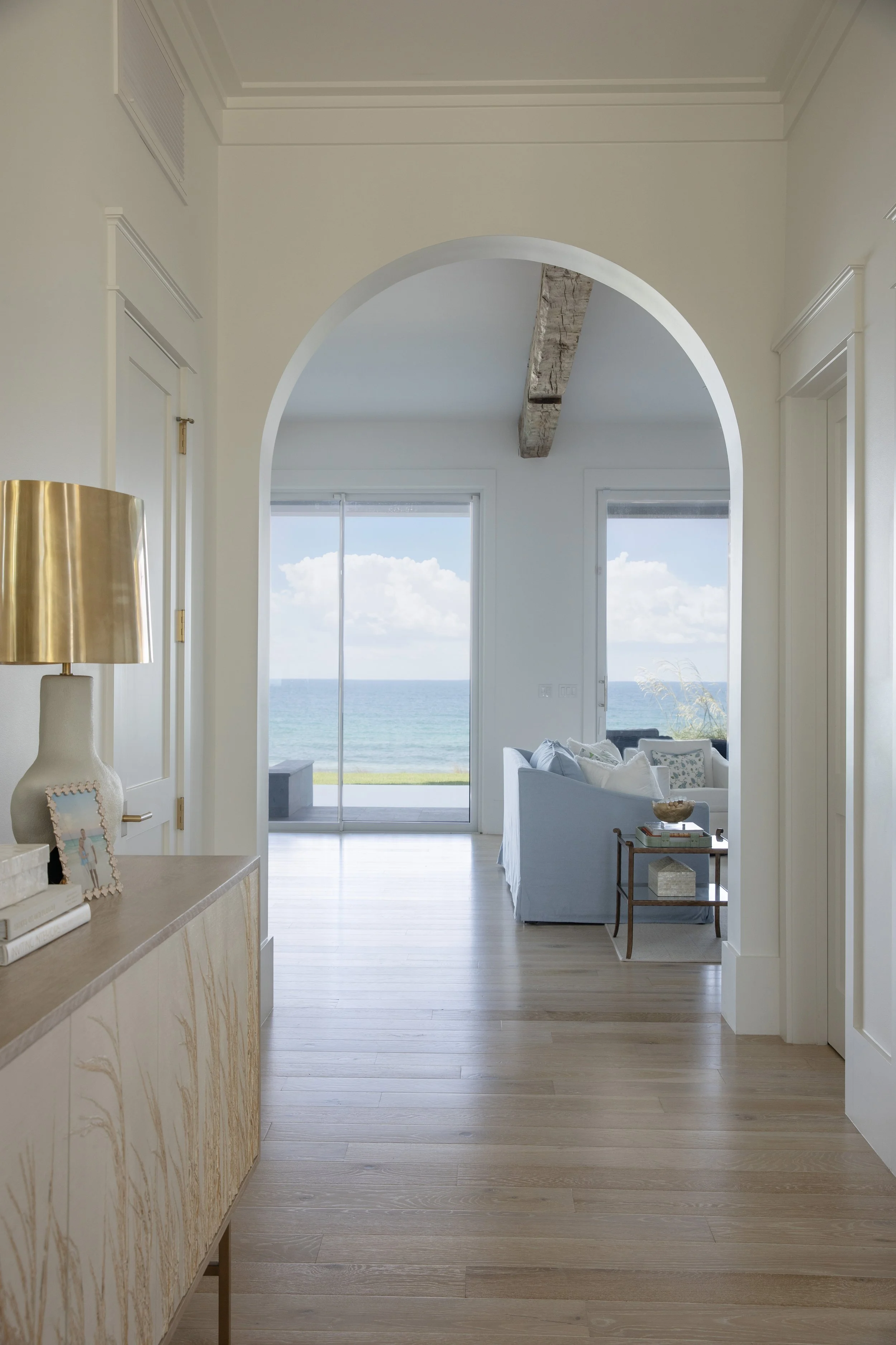 Arched hallway in a Blue Mountain Beach home by Cindy McCarley Designs, opening to a coastal living room with sweeping Gulf views
