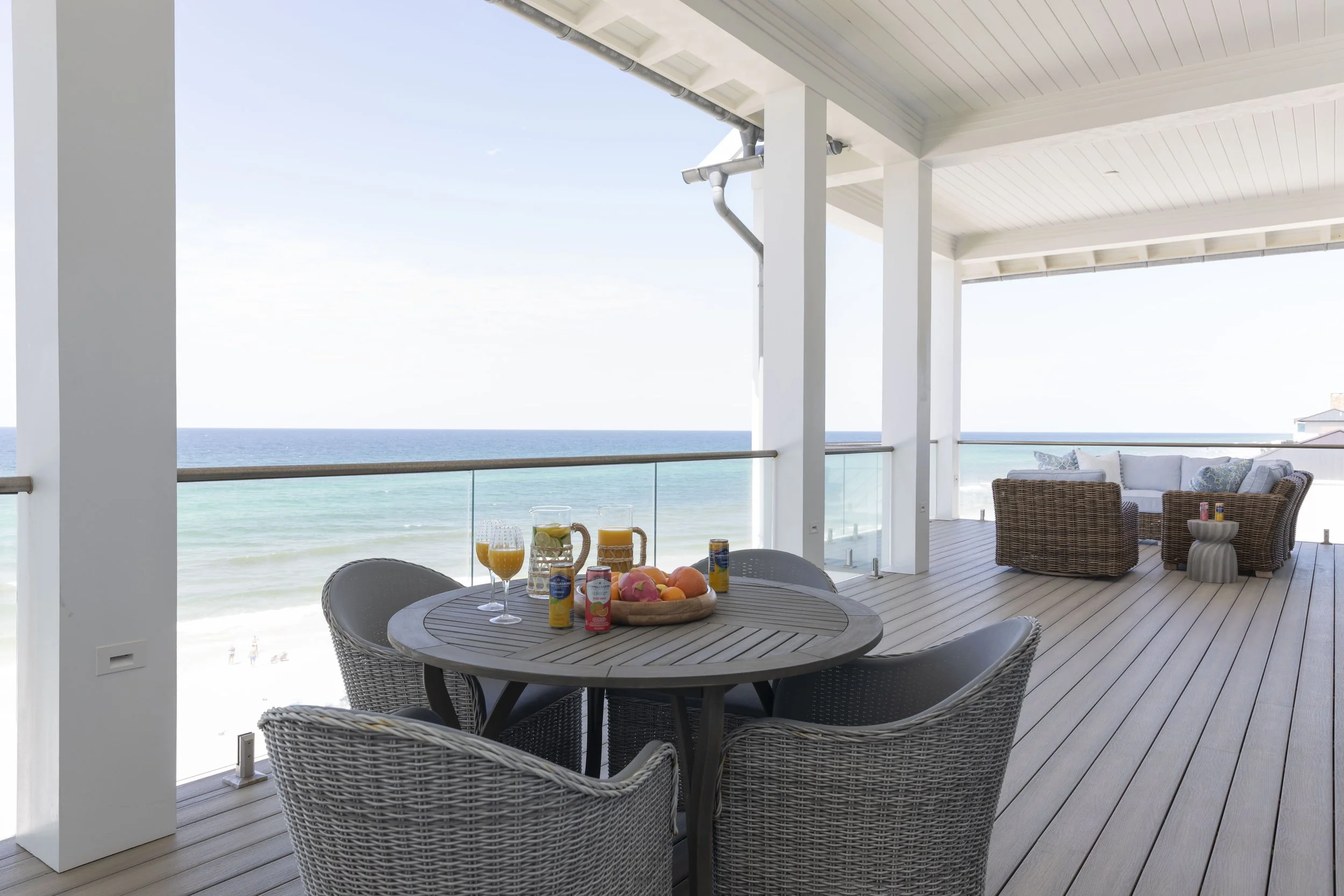 Covered outdoor living and dining space in Blue Mountain Beach by Cindy McCarley Designs, featuring woven patio furniture and panoramic Gulf views.