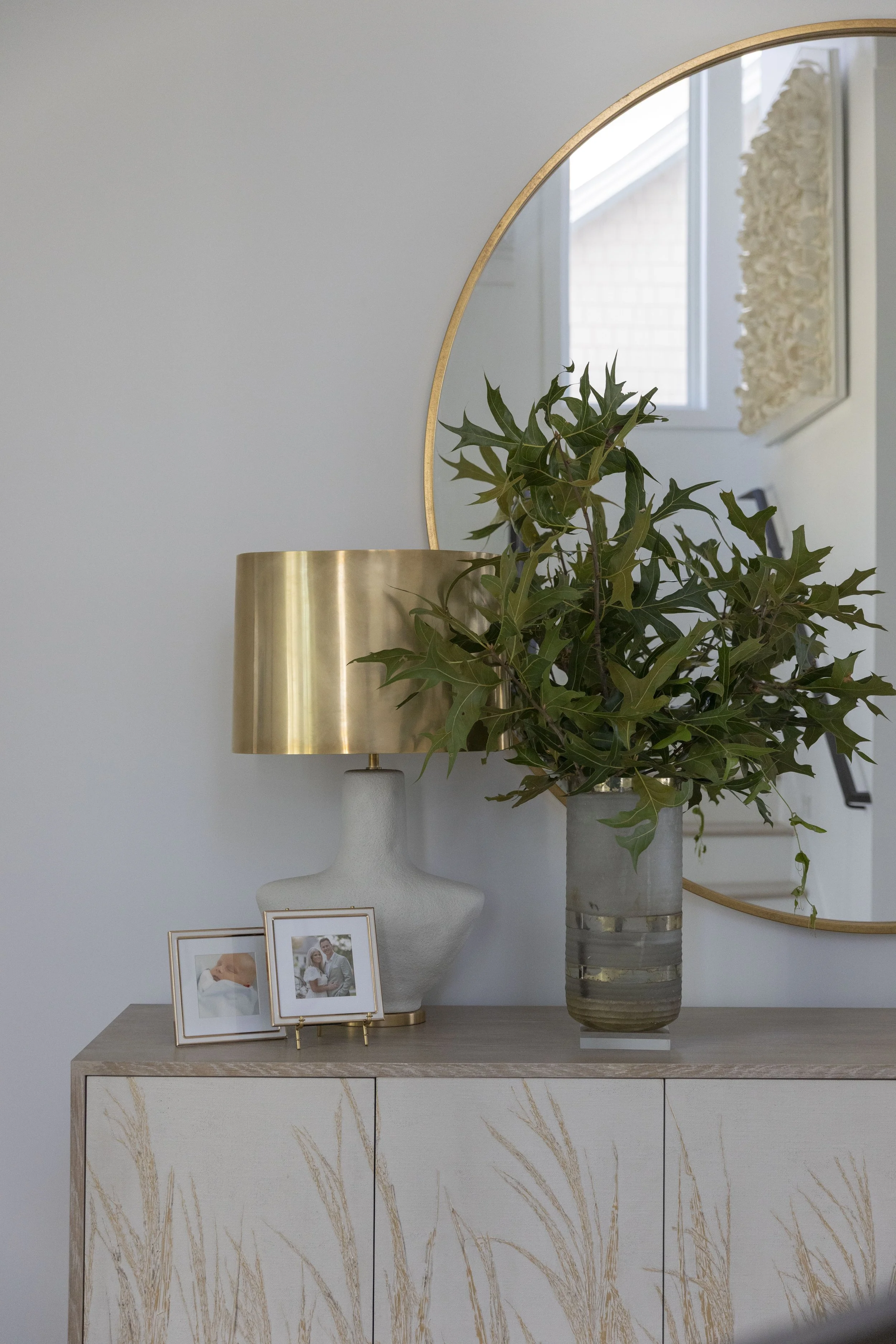 Styled entryway console in Blue Mountain Beach by Cindy McCarley Designs, featuring a round gold mirror, brass table lamp, textured cabinet and greenery.