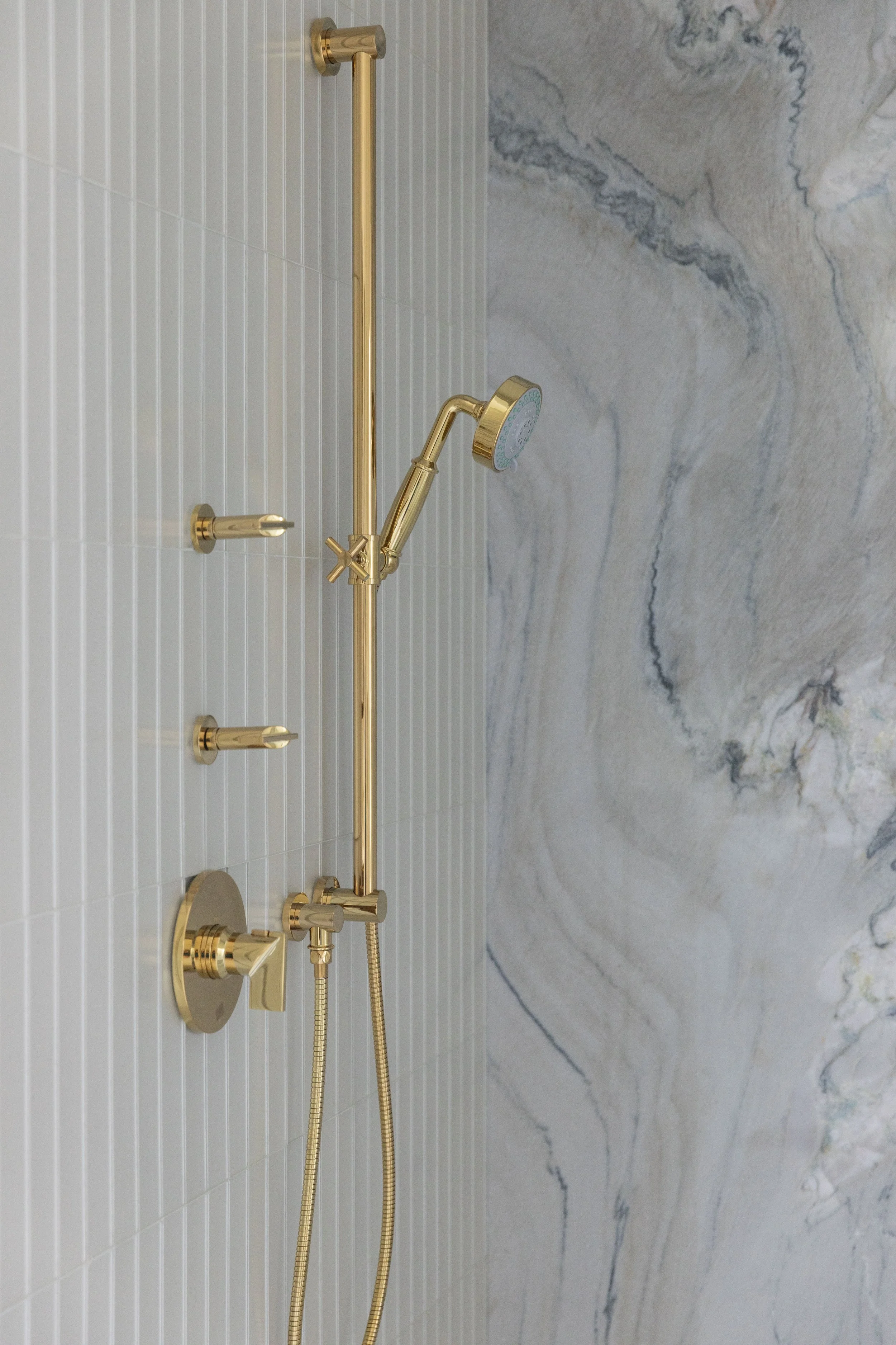 Luxury shower detail in Blue Mountain Beach by Cindy McCarley Designs, featuring polished brass fixtures, vertical tile and a dramatic marble accent wall.