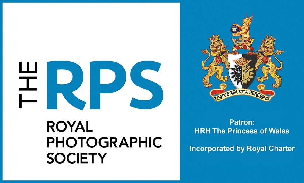 Logo of the Royal Photographic Society featuring a shield with a lion and a face, a crown, and the Latin motto 'Universa Vita Percepita' with text about the society and its patron, HRH The Princess of Wales.