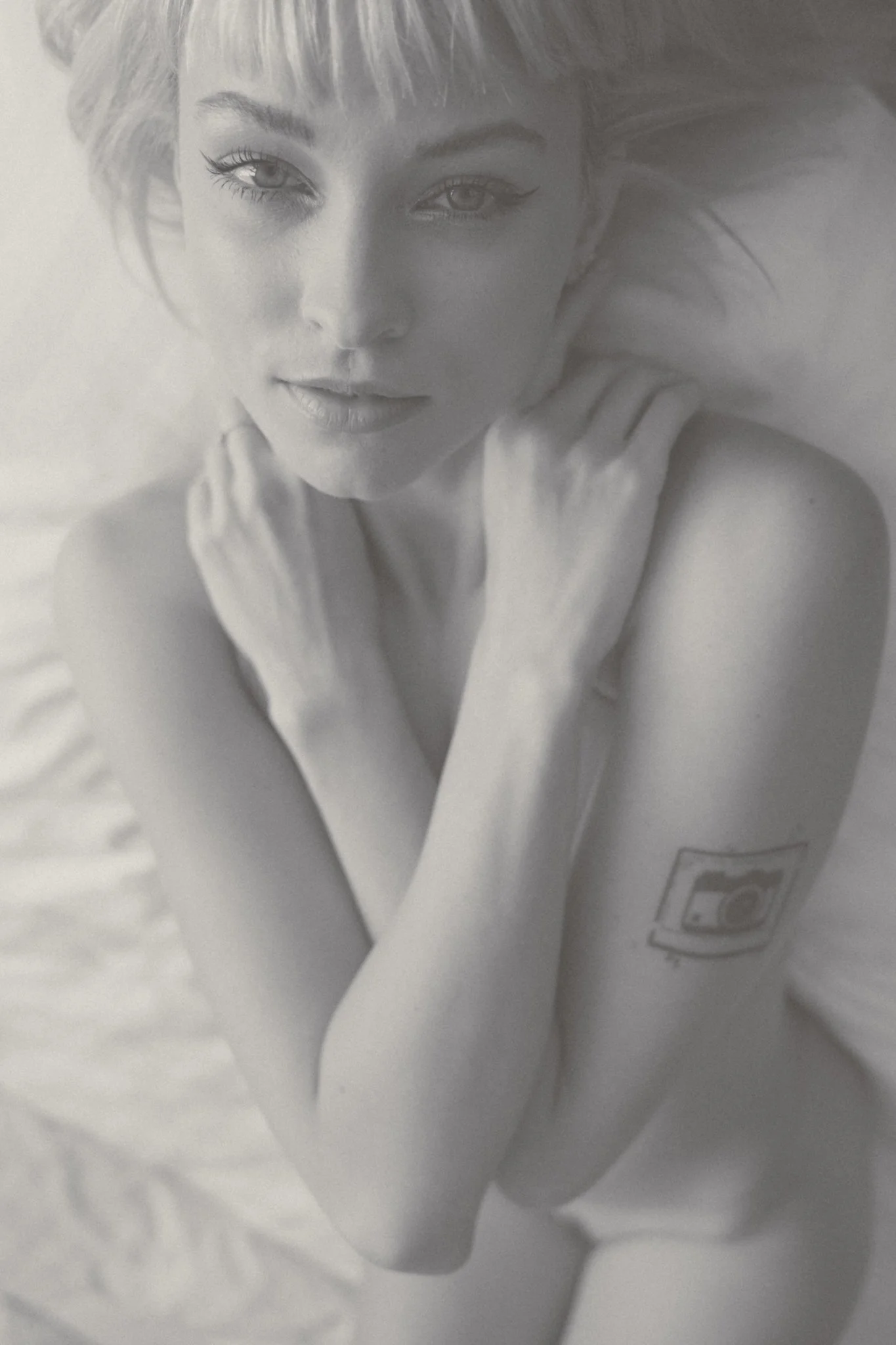 A black and white photo of a woman with short hair, resting her head on her hand, with a gentle smile.
