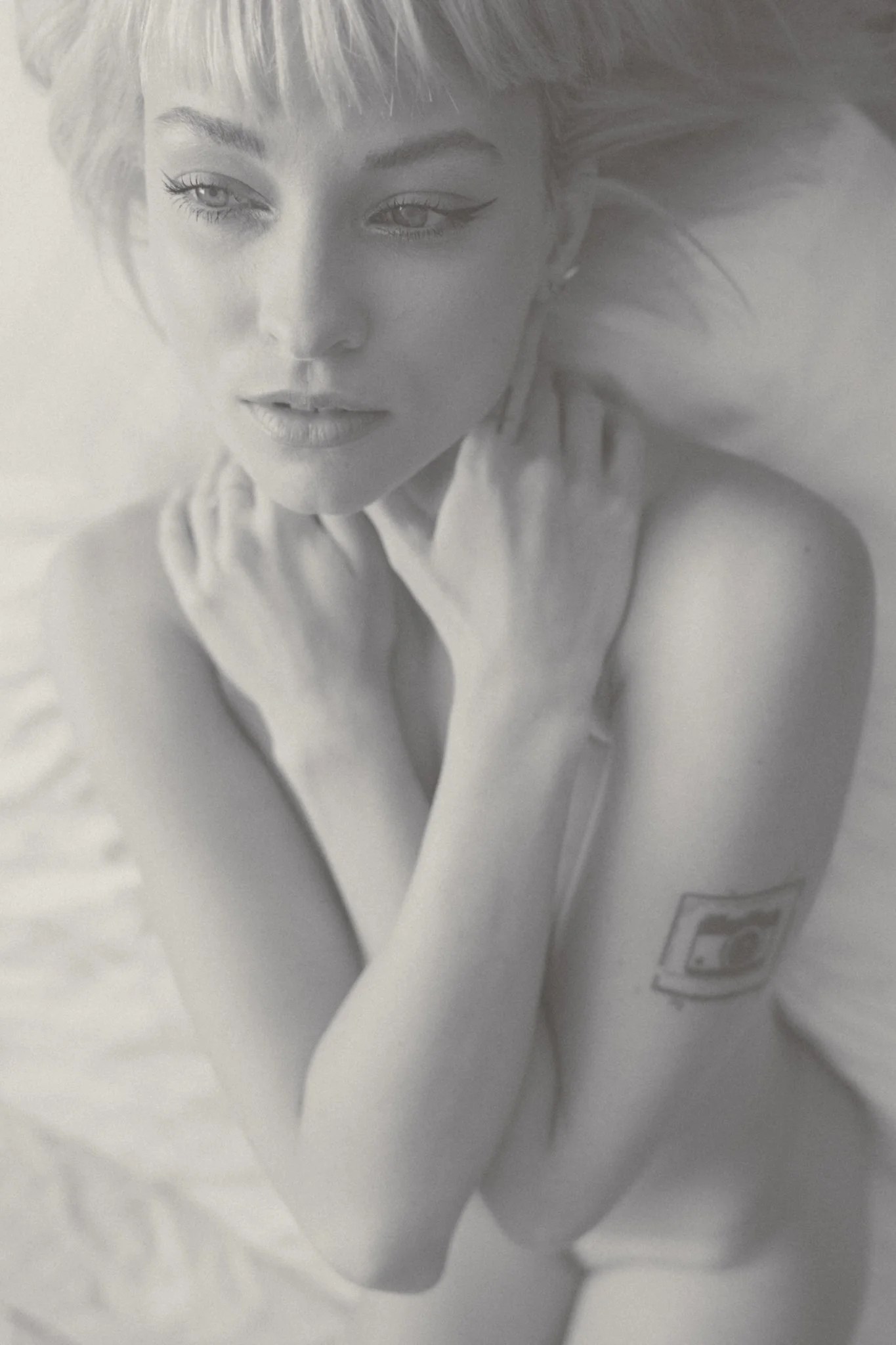 Black-and-white photograph of a woman with short blonde hair and eyeliner, resting her chin on her hand.