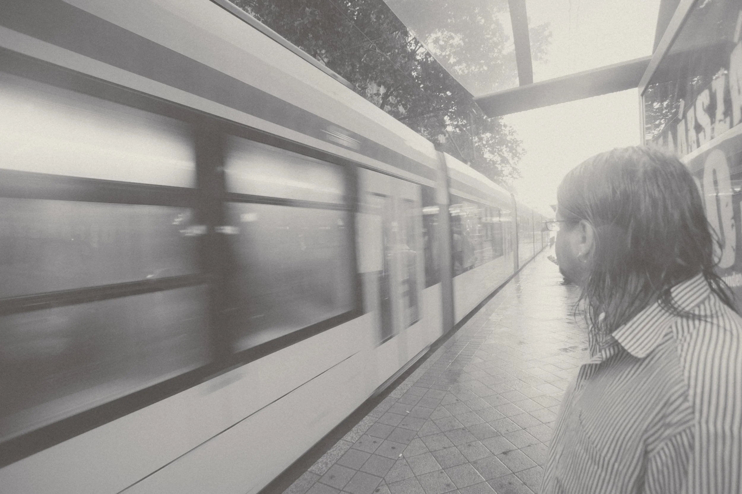 A person standing on a bus stop platform looking at a moving bus passing by.