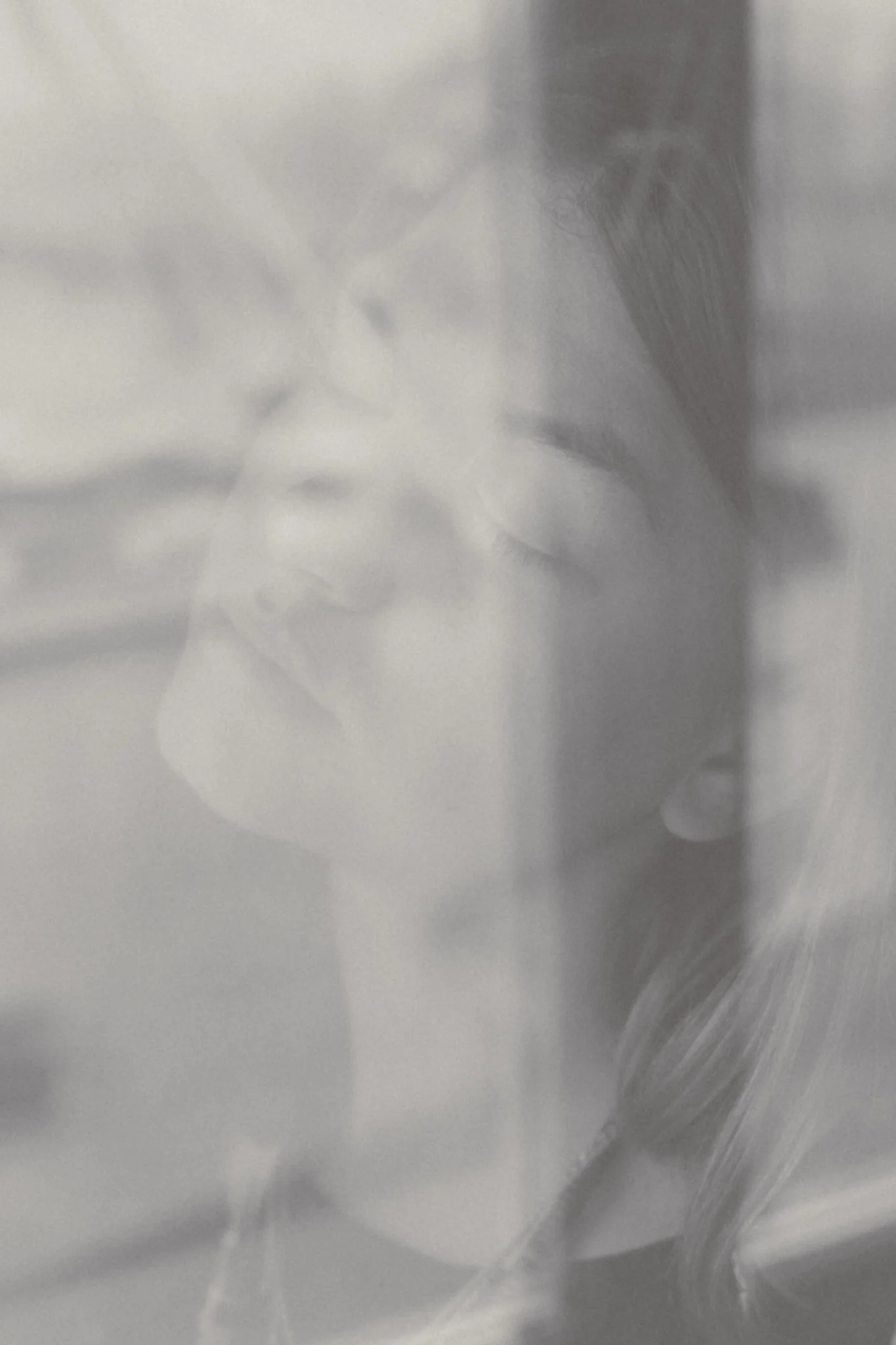 A faint, blurred, double-exposure photo of a woman with glasses and long hair, possibly holding her hand near her face.