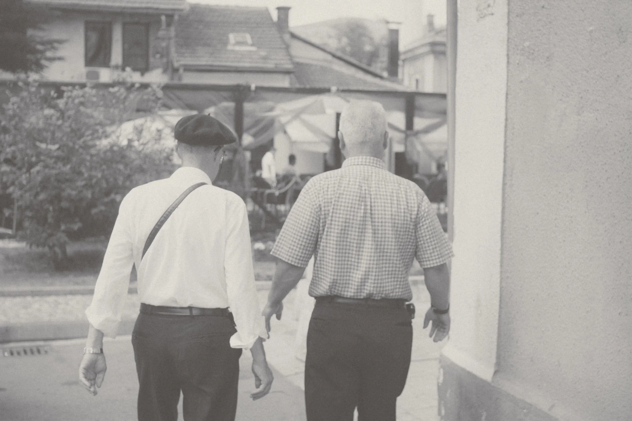 Two elderly people, a woman in a beret and a man, walking hand in hand on a city street.