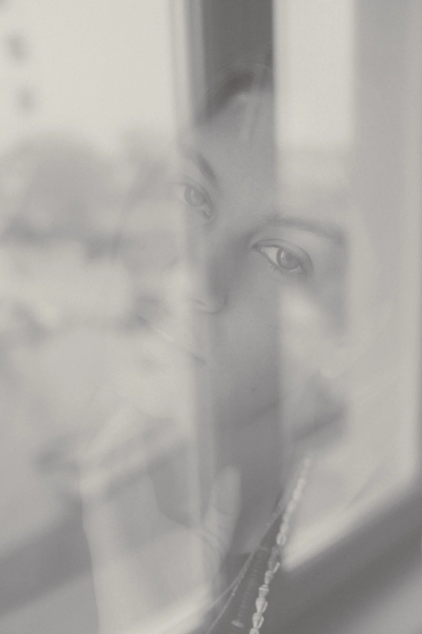 A person taking a selfie through a foggy or frosted glass with another image of a woman behind the glass, creating a layered effect.