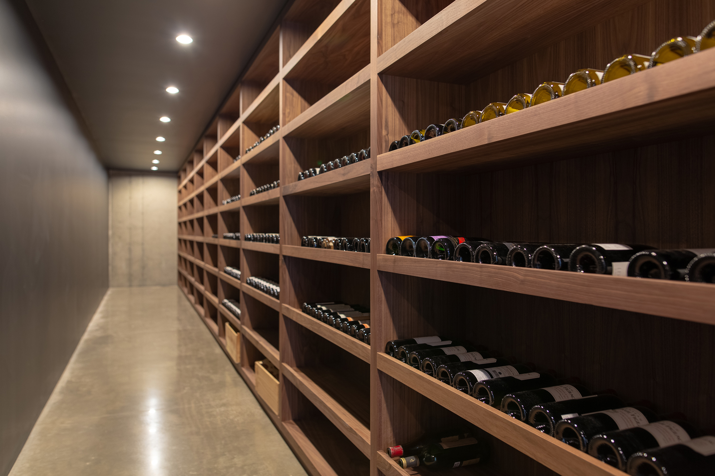 The basement wine cellar was designed to be passively cooled year-round. Custom walnut shelving warmed the minimal palette of polished concrete and soot black