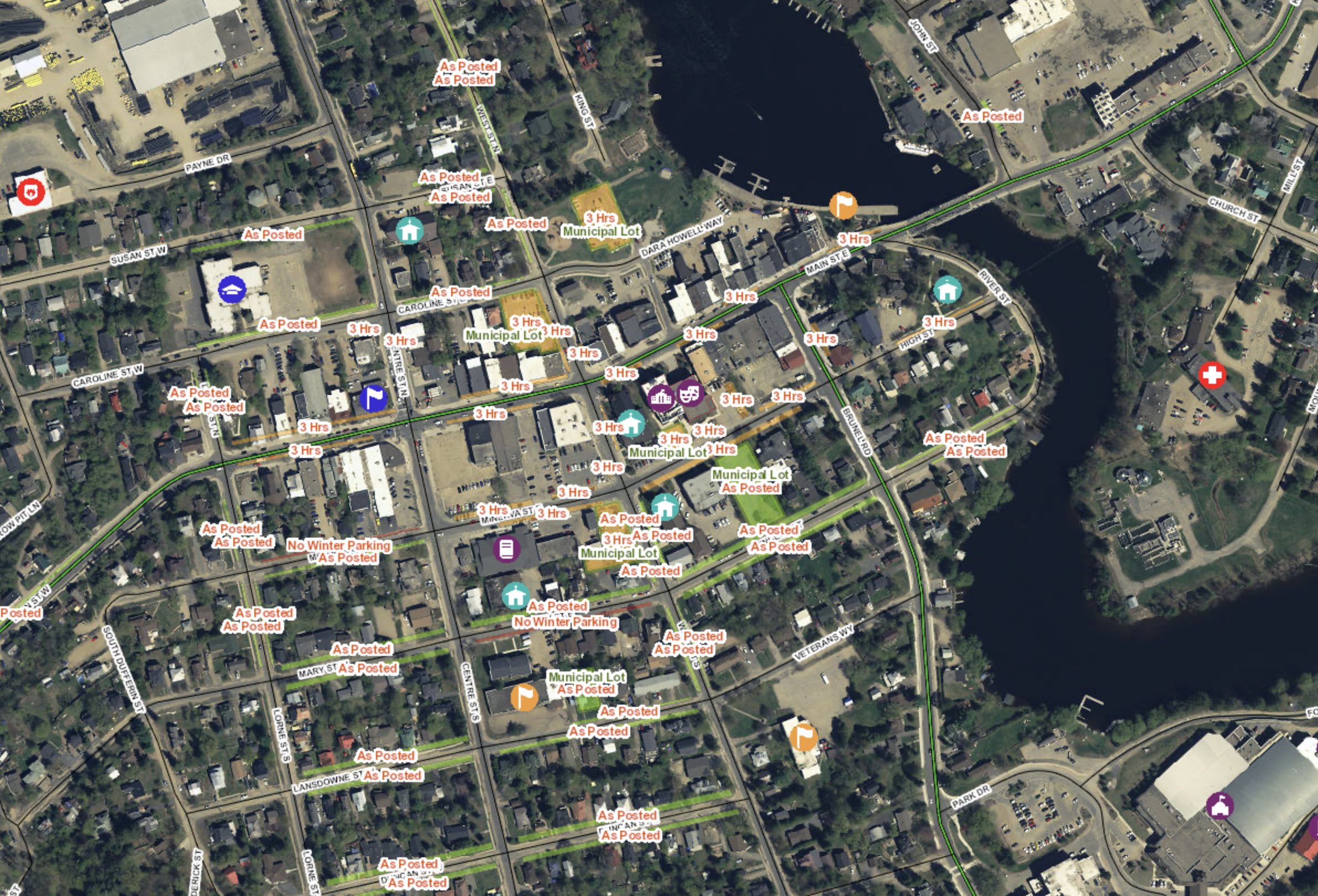 A satellite map of an urban area showing streets, buildings, parking lots, a water body, and various markers indicating parking, municipal lots, and posted notices.