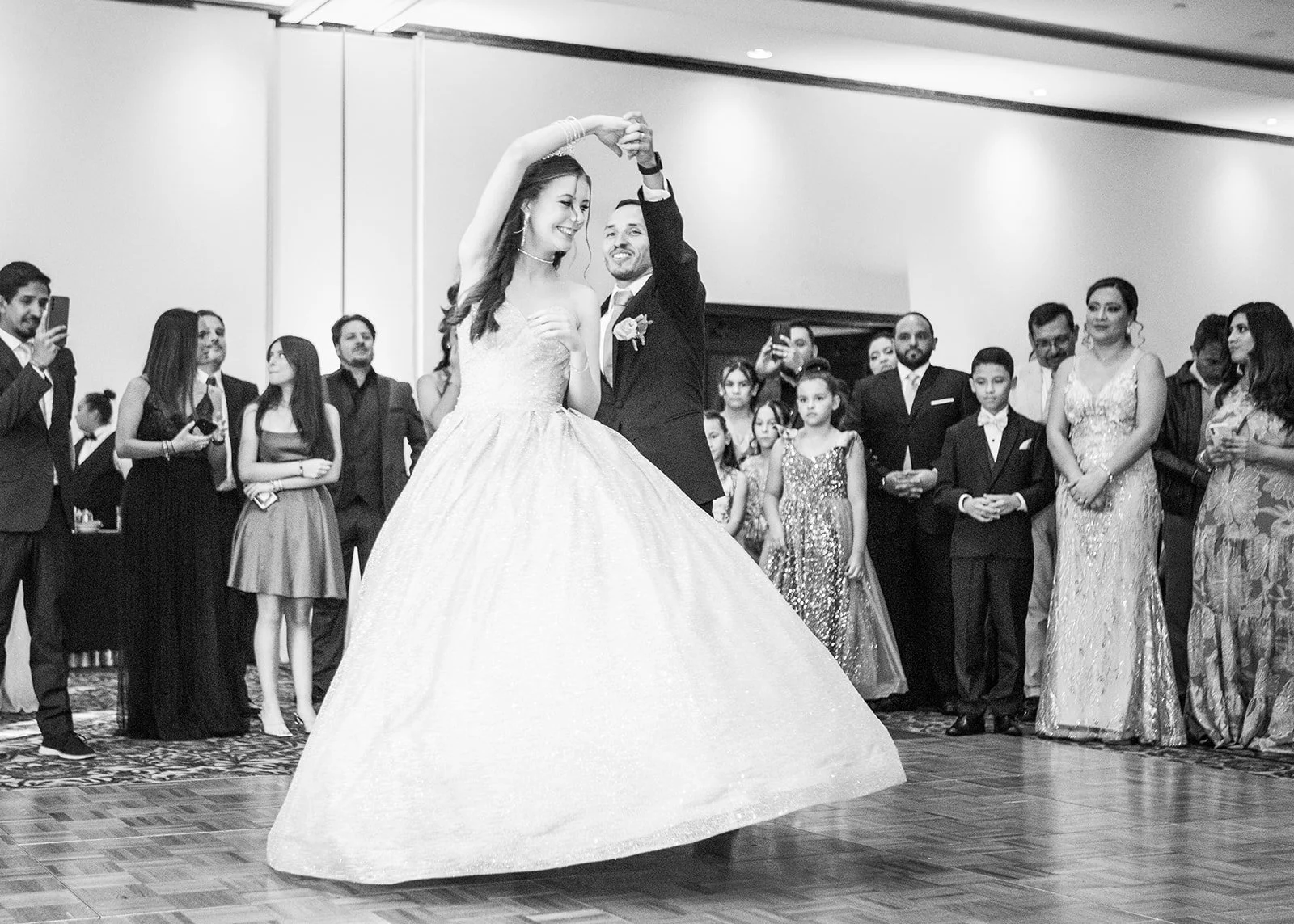 Fotografía en blanco y negro del baile del vals de una quinceañera en Guatemala con su vestido de gala ante la mirada de sus invitados.