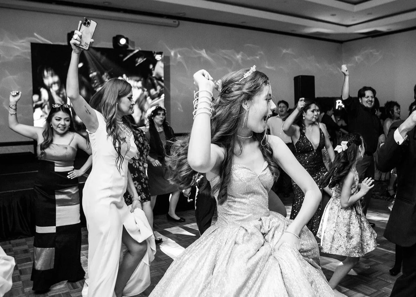 fotografía en blanco y negro llena de energía de la quinceañera y sus invitados bailando alegremente en la pista durante la recepción en Guatemala.