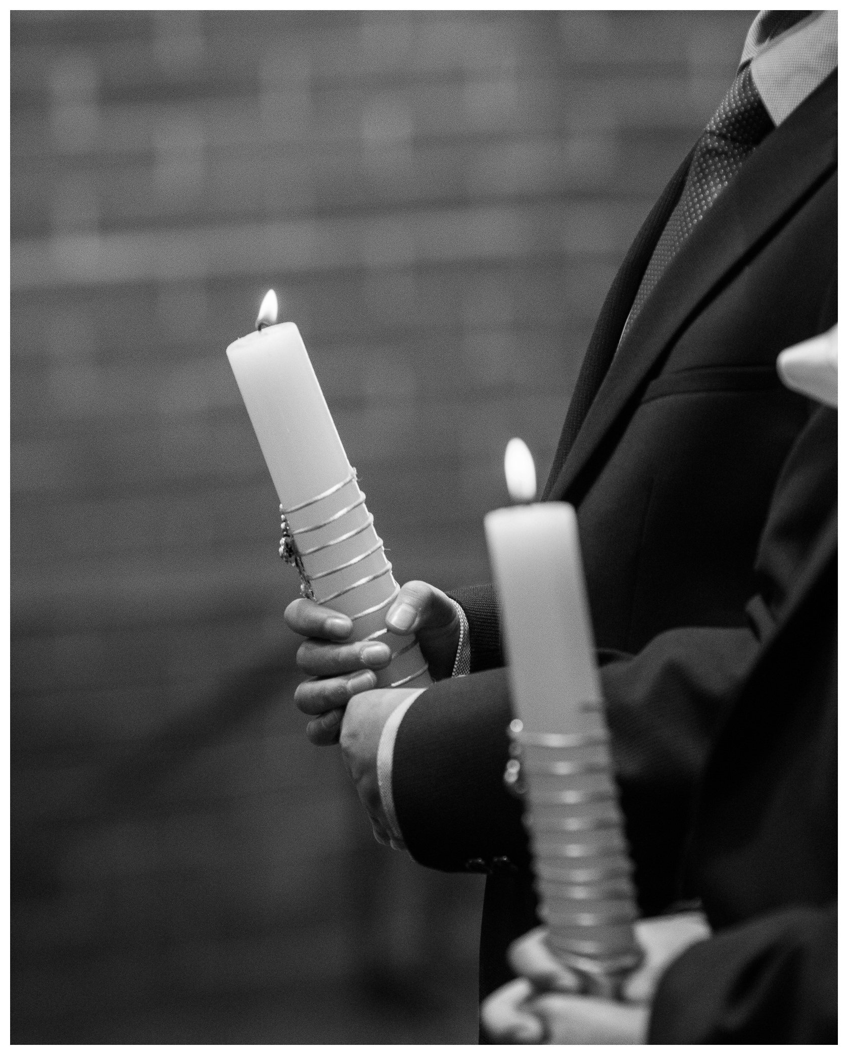 Primer plano en blanco y negro de las manos de un niño sosteniendo una vela de primera comunión encendida y decorada con un rosario durante la misa.