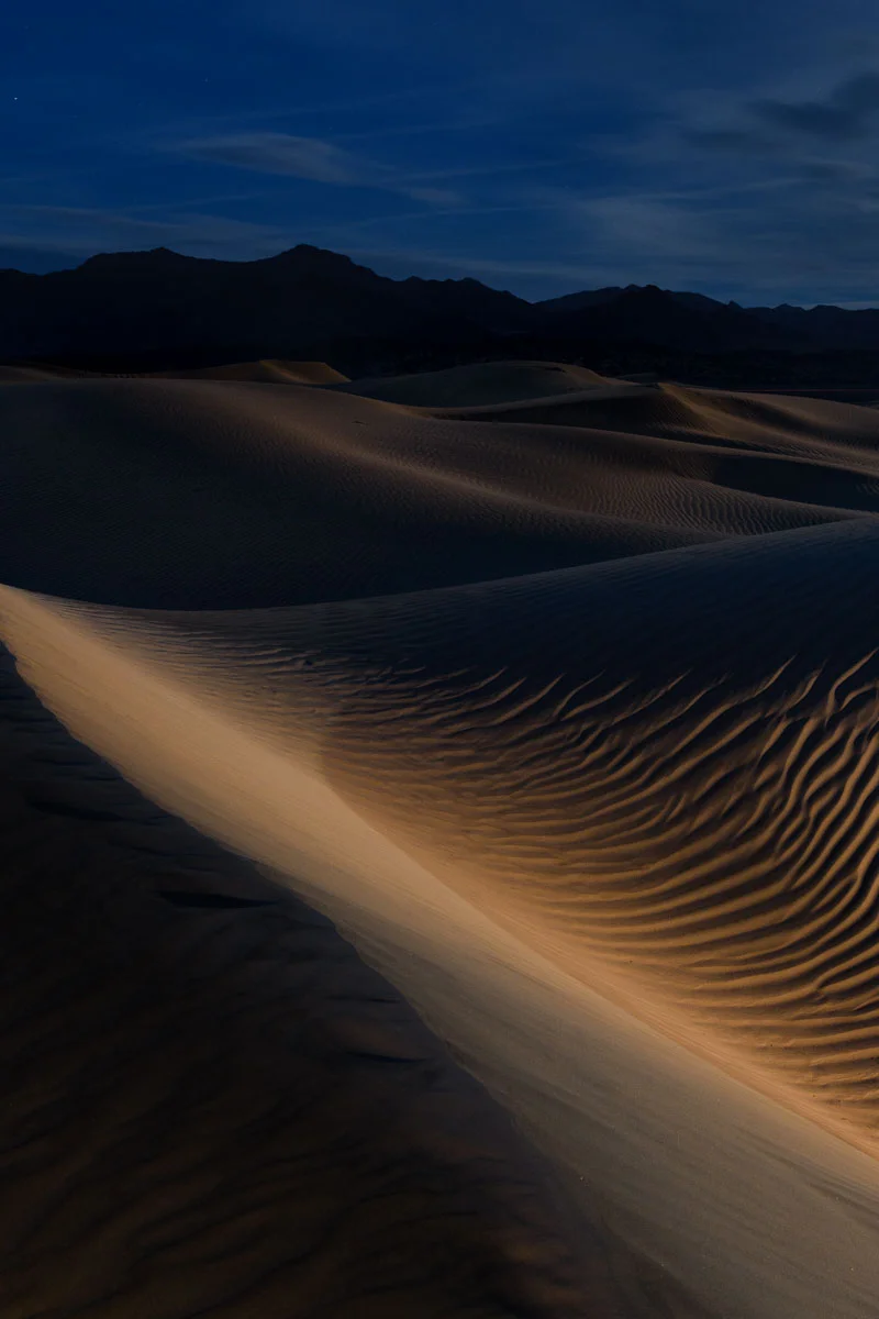 Mesquite Flat Sand Dunes, Death Valley National Park. The moon is low in the sky and the ambient exposure is intentionally underexposed for effect. For the middle-ground dunes, warmth, exposure and contrast were boosted using a local adjustment brush in Lightroom. An example of the malleability of files from this camera. Nikon D850, Nikon 24-120mm f/4 lens at 34mm, and Luxli Constructor LED light at 3200 K on the lowest setting, placed at the toe of the foreground dune. 30 seconds, f/10, ISO 800.