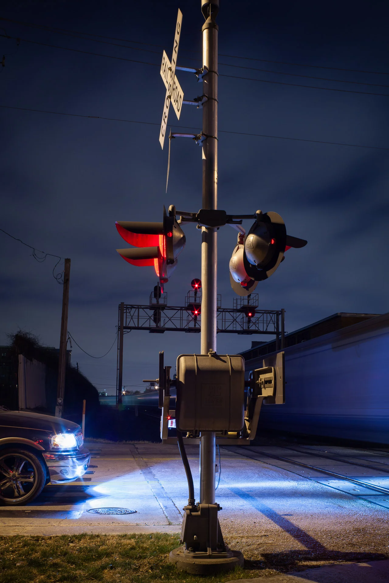An SUV waits at the rail crossing, Houston, Texas, 2011. Canon 5D Mark II with a 50mm f/1.4 lens. 15 seconds, f/8, ISO 200. Everything came together in this spontaneous image–– the timing of the train, the composition and the lighting. The red warning light at the crossing provides a color accent and the cool xenon headlights of the SUV illuminate the passing train.