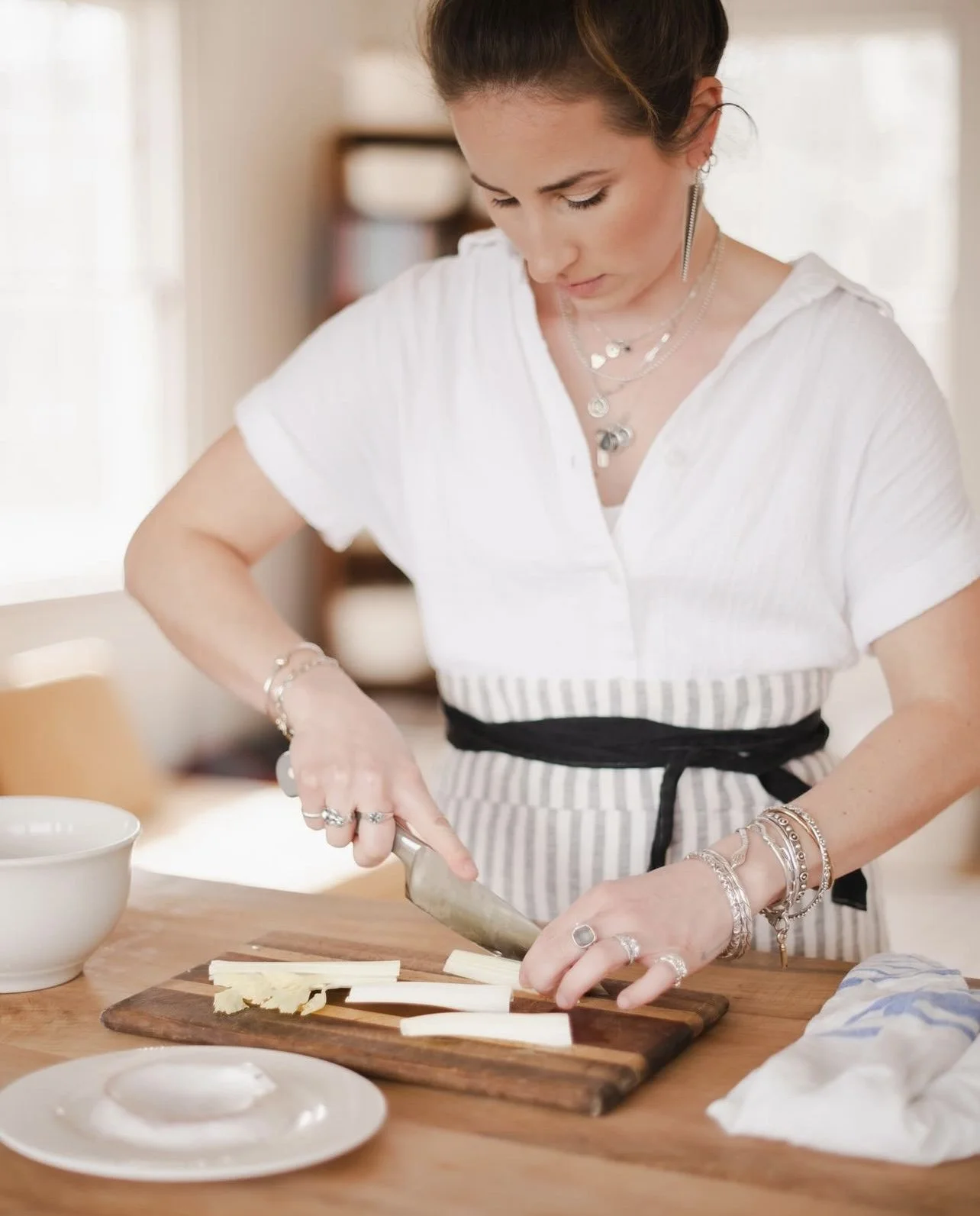 Chef slicing vegetables on a cutting board in a kitchen, wearing a white shirt and an apron.