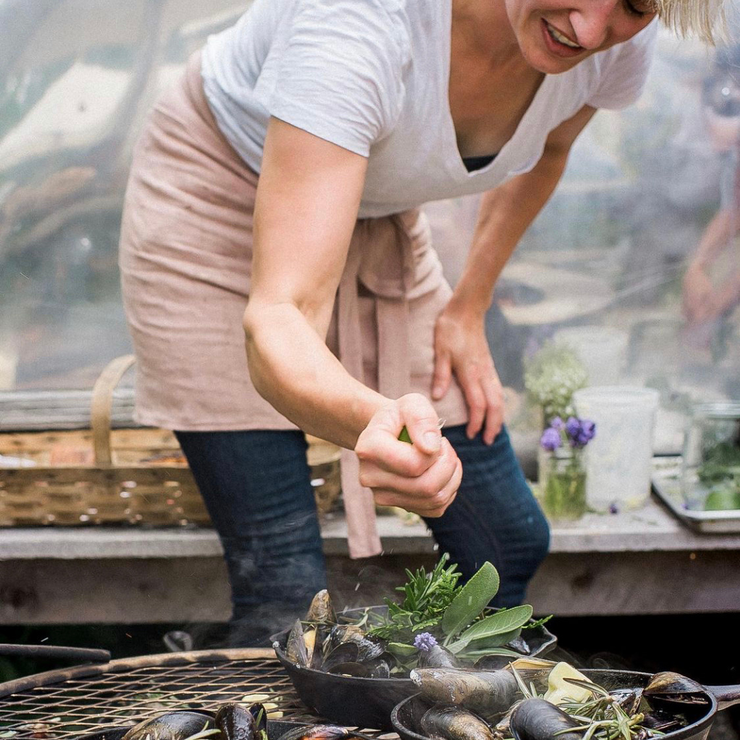 Woman cooking mussels with herbs and garlic on a grill.  Linen apron shown.