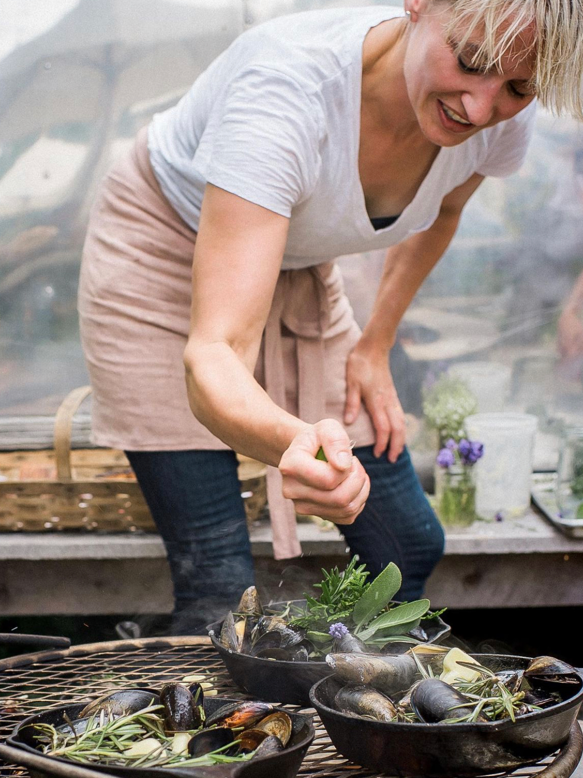Chef wearing an Amphitrite Apron cooking, working with mussels and herbs in a garden.