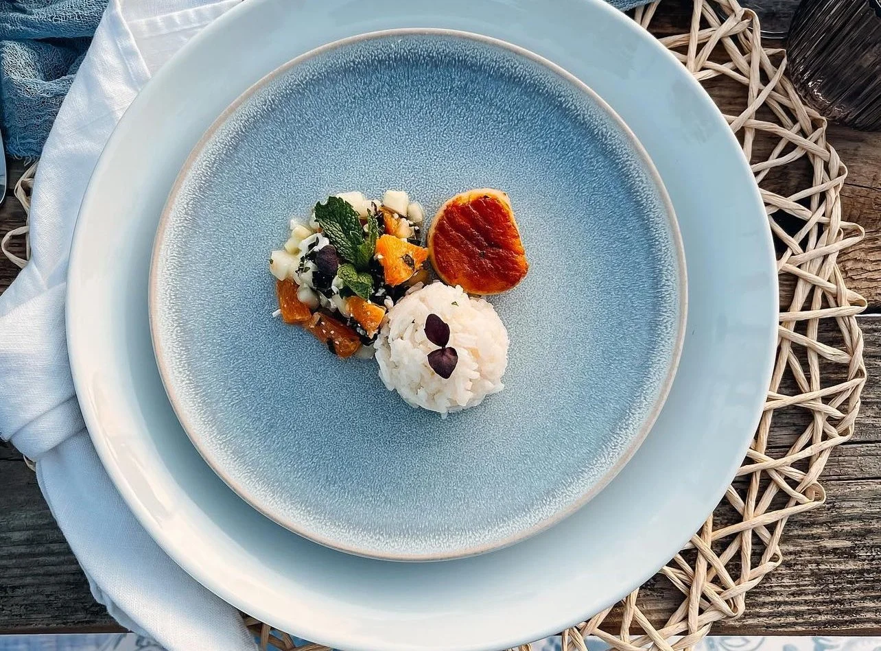 Plate with seared scallop, rice ball, and vegetable medley on blue dishware.