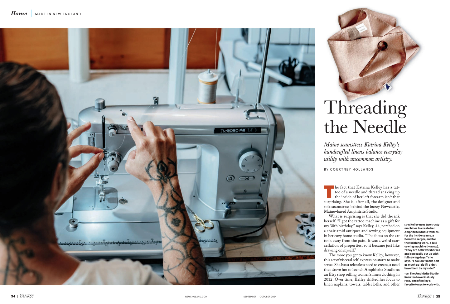 A person with tattoos sewing on a sewing machine in a workspace. The room has a wooden wall, with sewing supplies nearby. A pink linen textile and scissors are on top of the page.