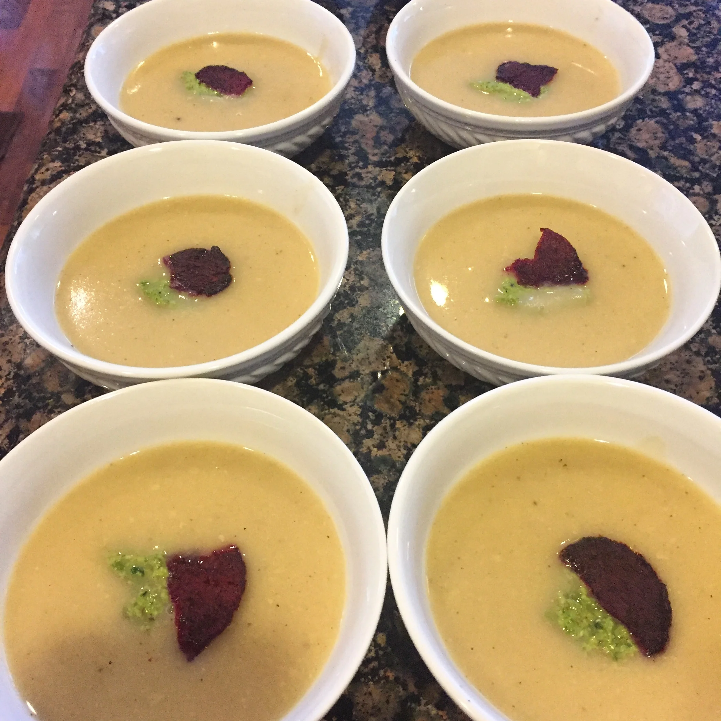 Cream of cauliflower ginger soup with spring pea pesto and topped with a beet chip.