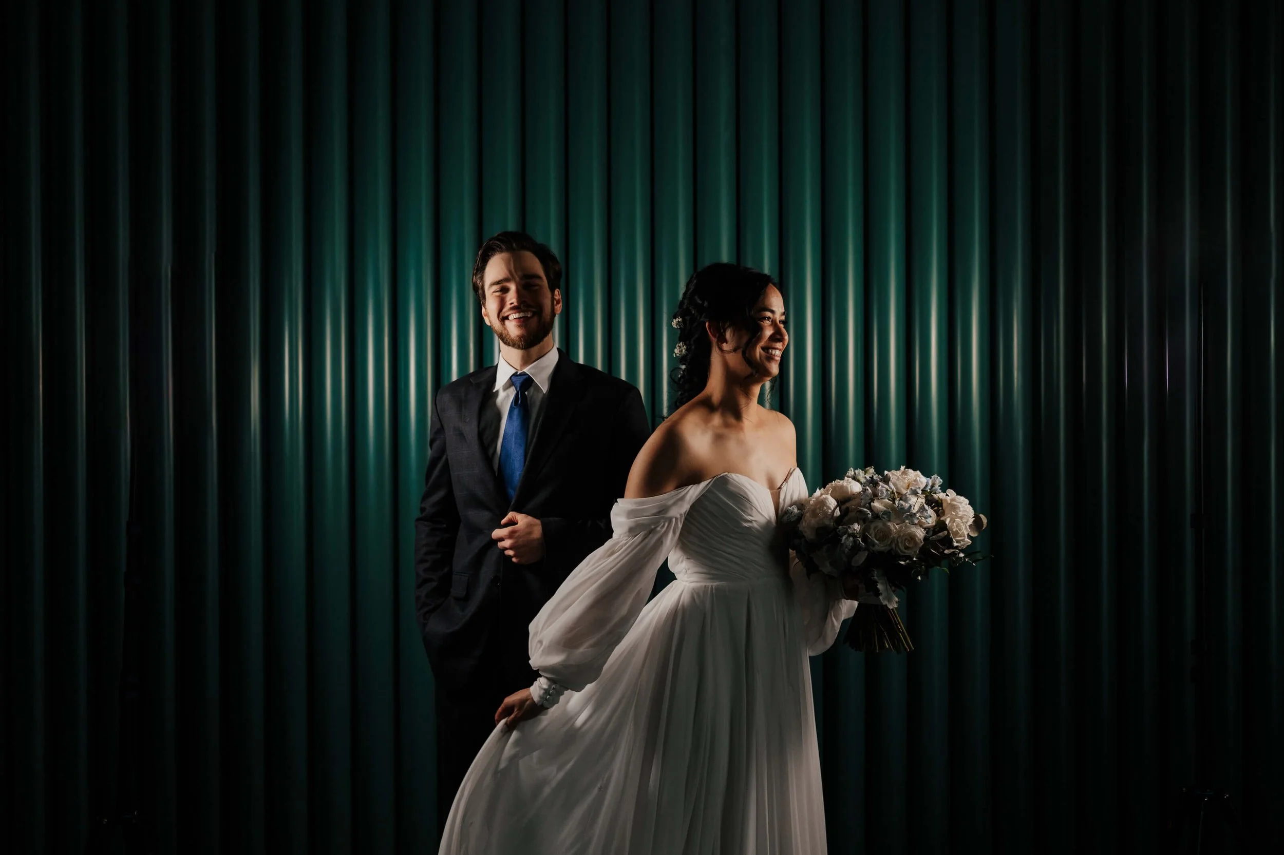 Leona Road wedding photographer Grand Rapids Michigan editorial bride with bouquet and groom laughing against teal backdrop, best luxury West Michigan wedding photography