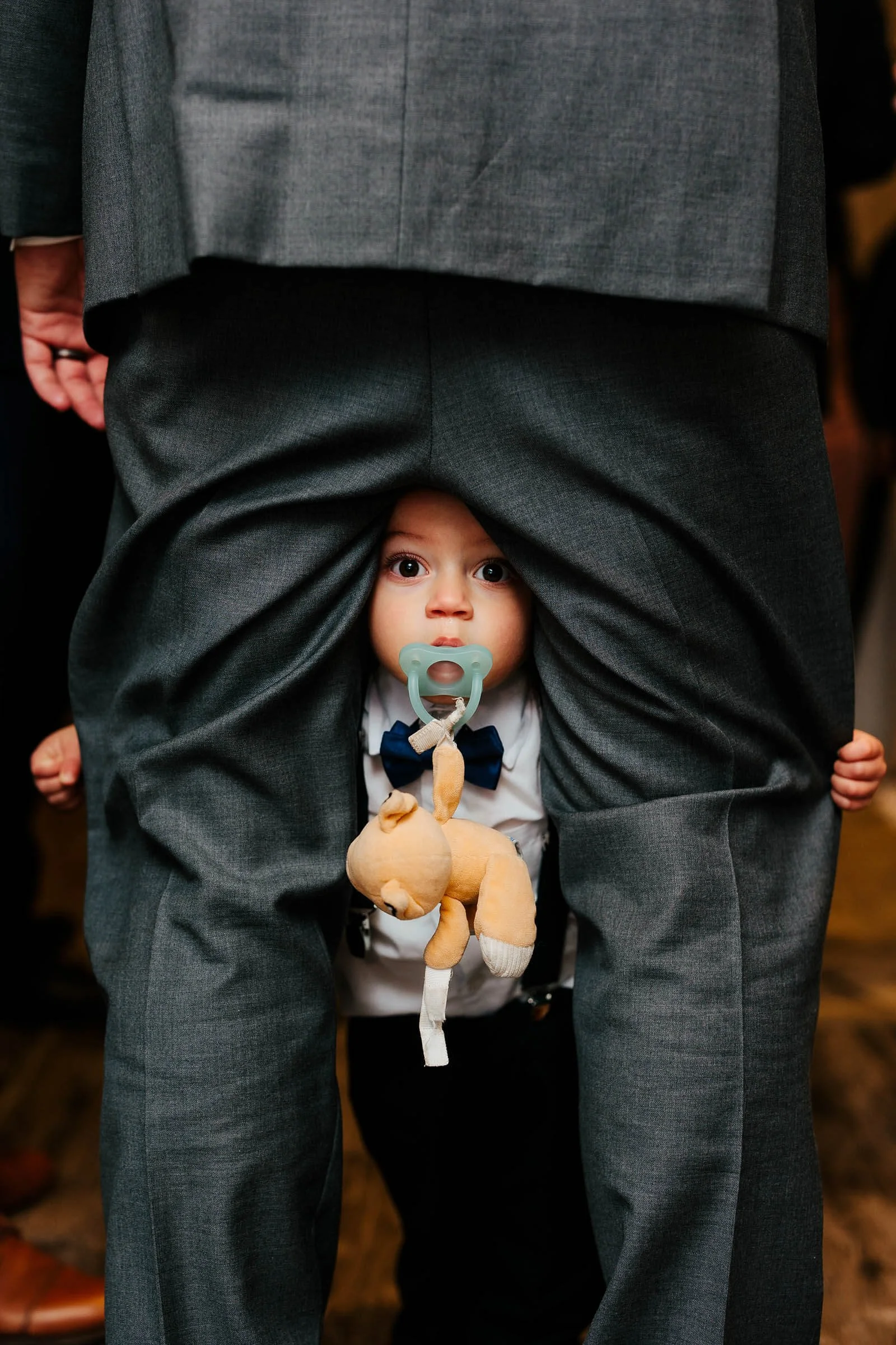 Lansing Michigan wedding photographer candid ring bearer toddler peeking through groomsman legs, MSU Horticulture Garden wedding