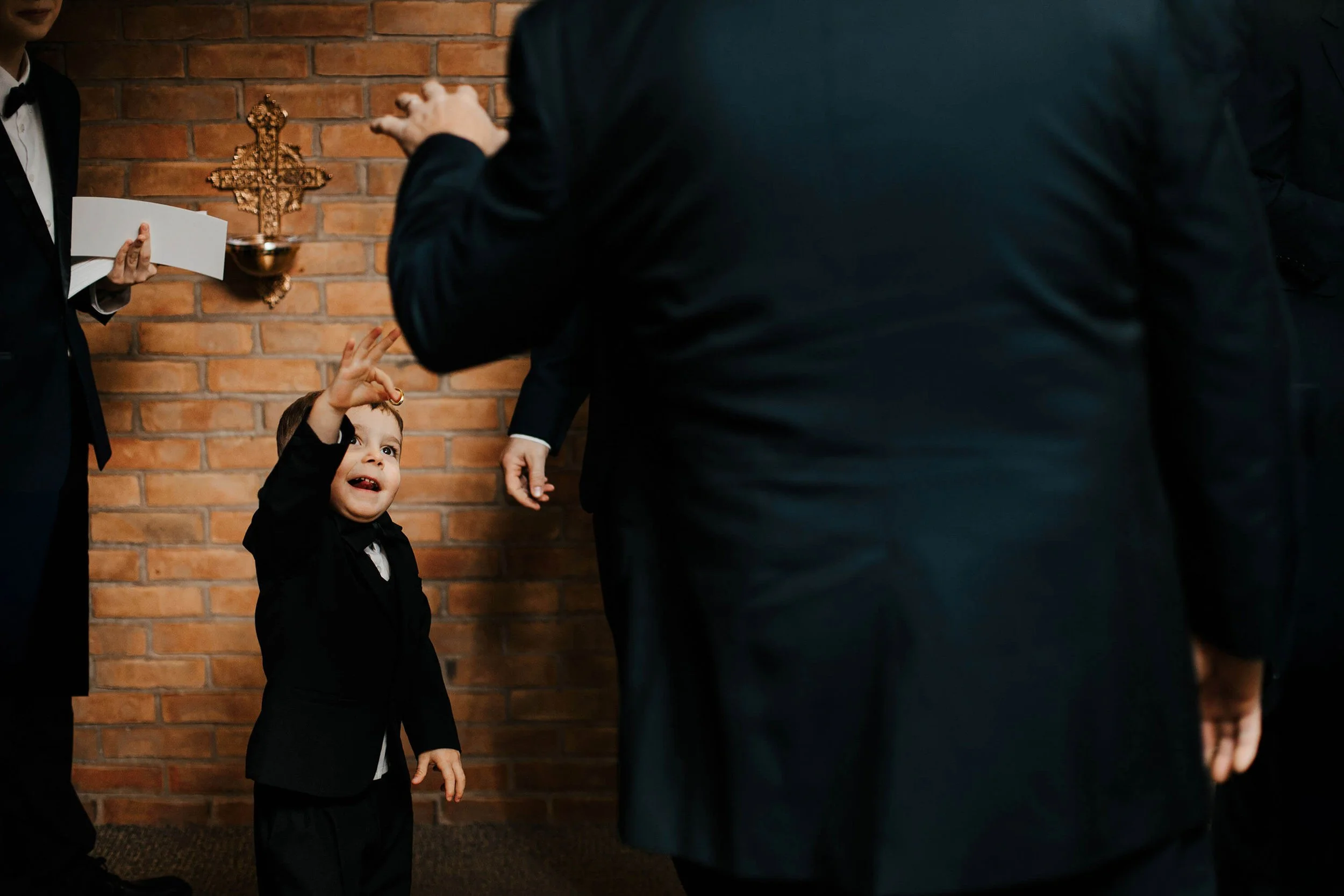 Illinois wedding photographer candid ring bearer toddler reaching up excitedly during church ceremony, Pipers Banquet Hall Aurora top Midwest wedding photography