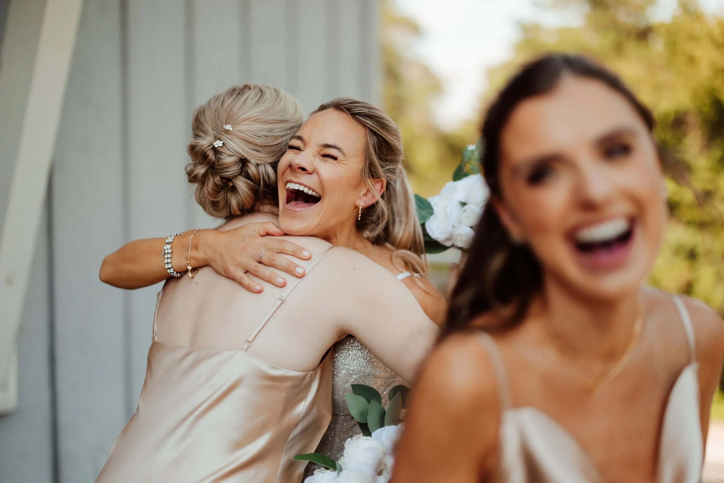 Bride laughing and hugging a bridesmaid during wedding day celebrations at Leona Road in Grand Rapids, Michigan