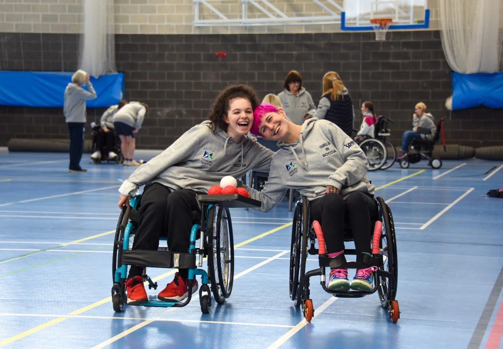 Two girls on the boccia court smilng for camera and with arms around each other