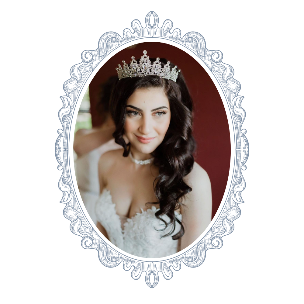 A young woman with long dark curly hair wearing a tiara and a white lace wedding dress, smiling softly in a portrait setting.