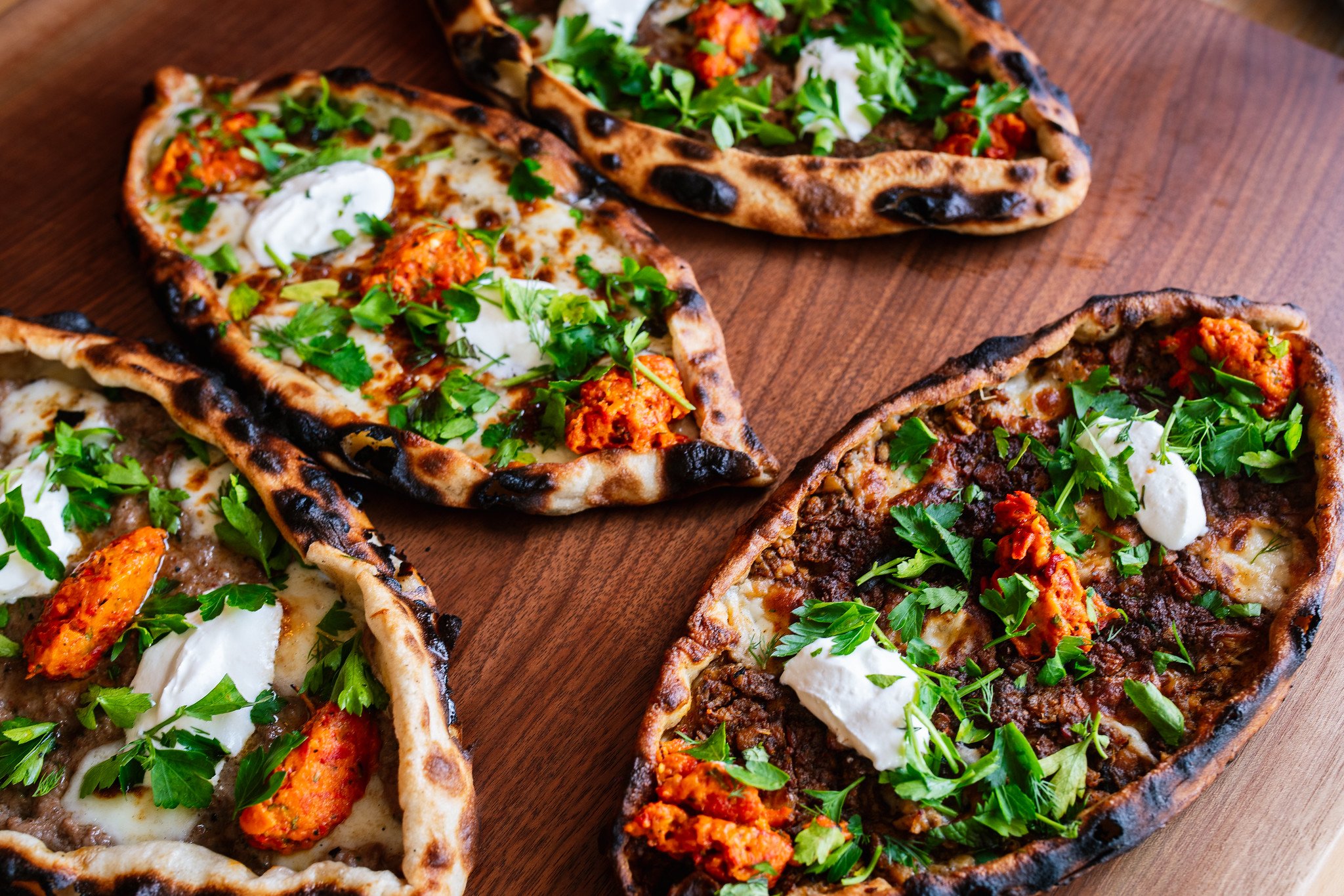 Four different types of stuffed naan bread topped with herbs on a wooden surface.