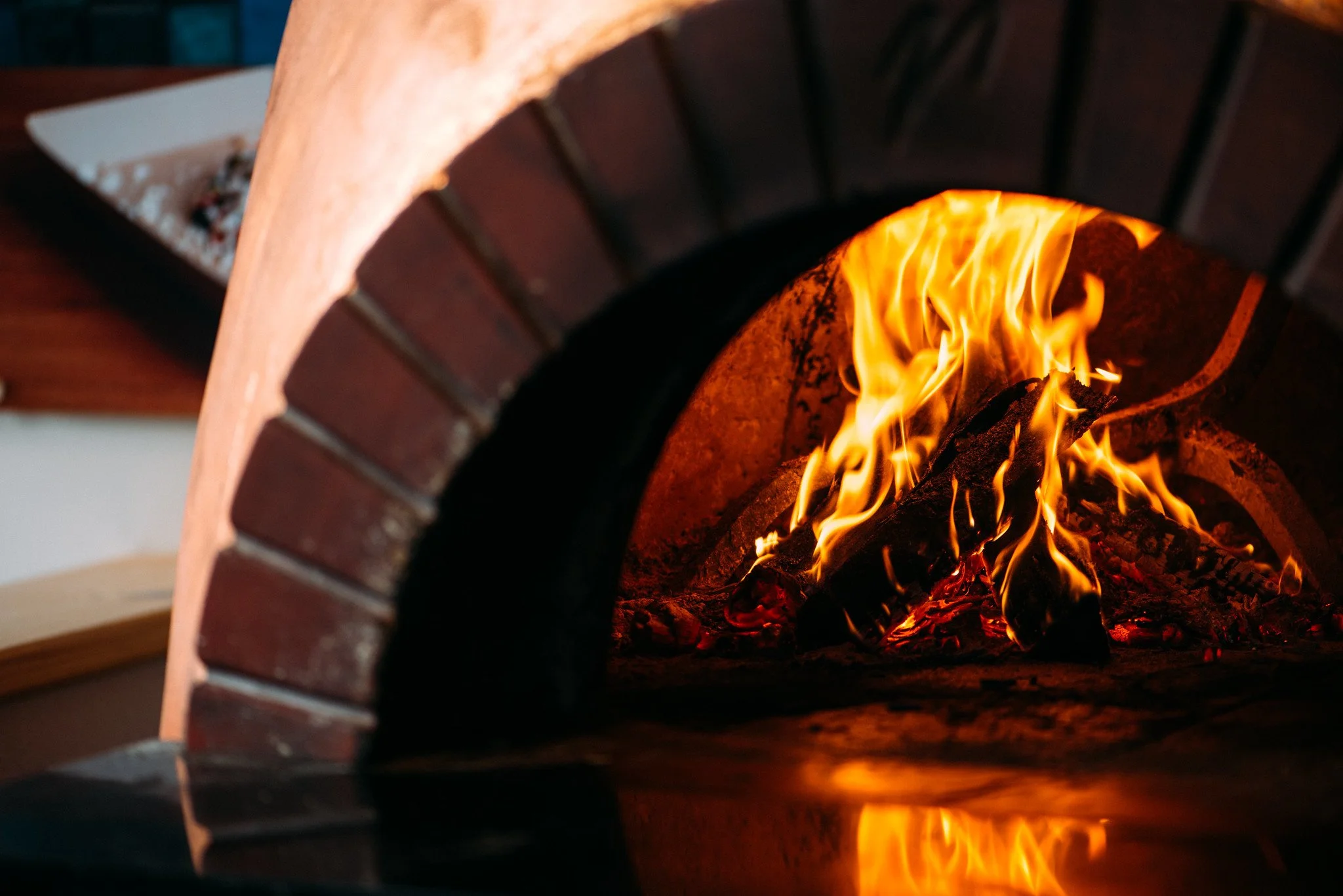 Close-up of a wood-fired brick oven with a burning fire inside.