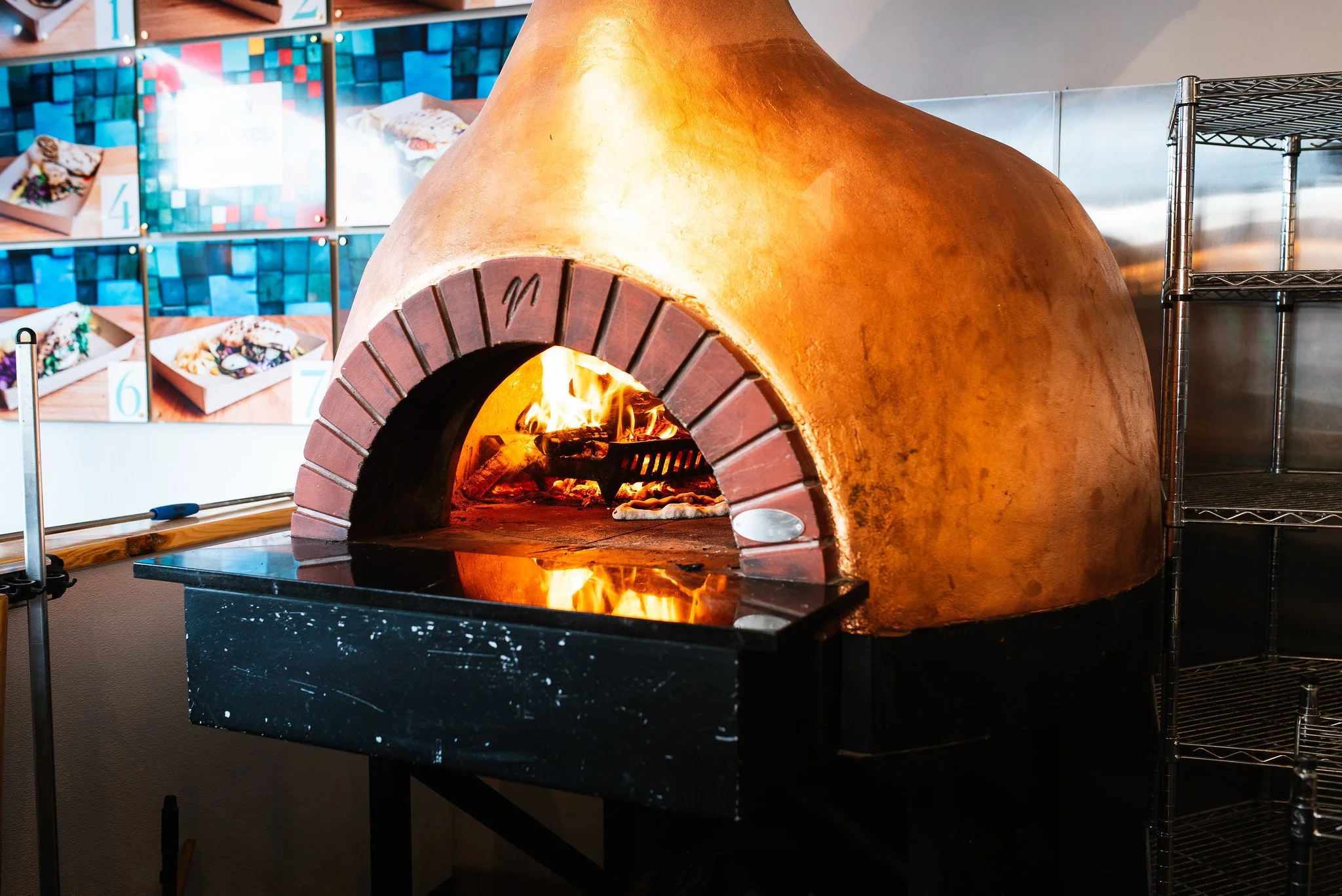 A traditional wood-fired oven with a fiery interior, made of brick and clay, on a black marble countertop, in a kitchen or restaurant setting.