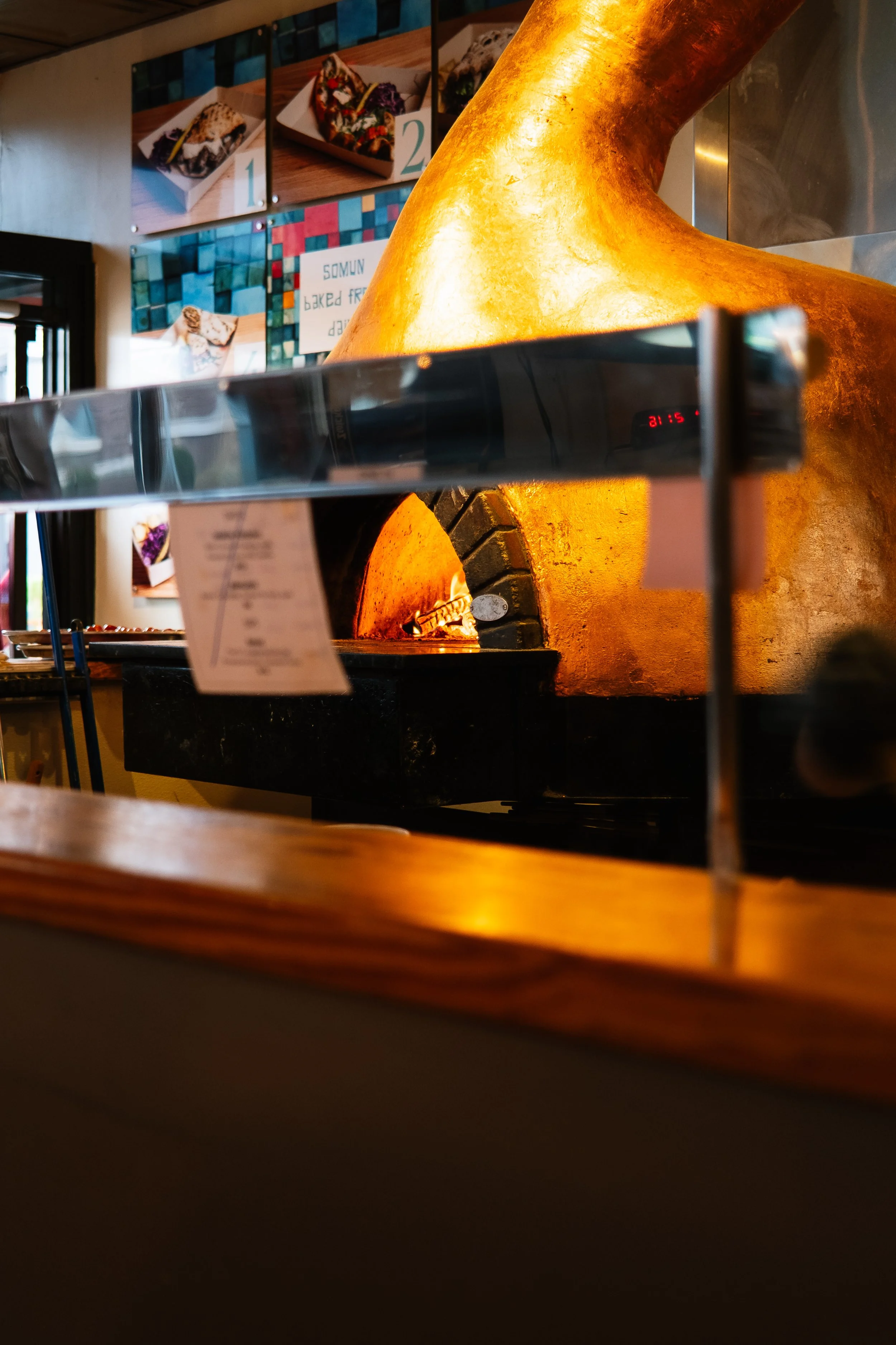 A large, golden, domed pizza oven with a fire inside, in a restaurant or bakery setting.