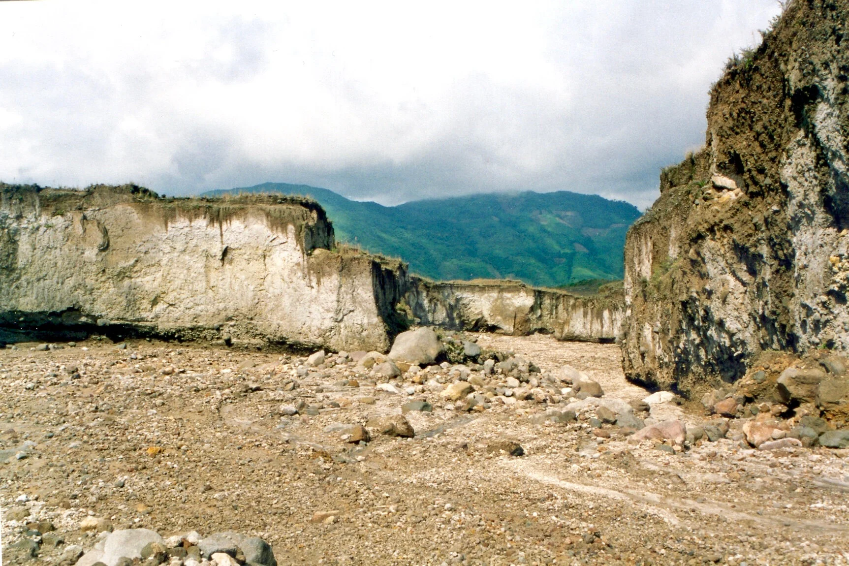   Sur ce cliché, à droite, on observe le dépôt volcanique emballant en vrac blocs, lapillis et cendres. L’eau a entaillé celui-ci et a dégagé les blocs et galets accumulés en pavage dans le fond du ravin tandis que les cendres et les ponces se sont accumulées en terrasses (gauche du cliché  