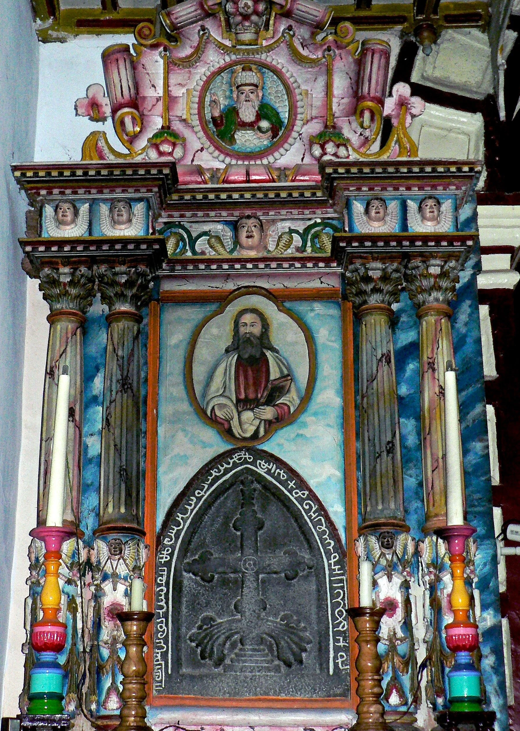    Autel nord : l’image de Dieu s’inscrit en médaillon dans la partie supérieure du retable. Il est séparé du monde terrestre par la ligne des anges. Le Christ est ici plutôt d’inspiration orthodoxe – Christ pantocrator – représenté dans un médaillon inscrit sur fond de ciel. Il s’élève au dessus d’une dalle (75cm x 58cm) comportant la “Croix Saint-Thomas”.   