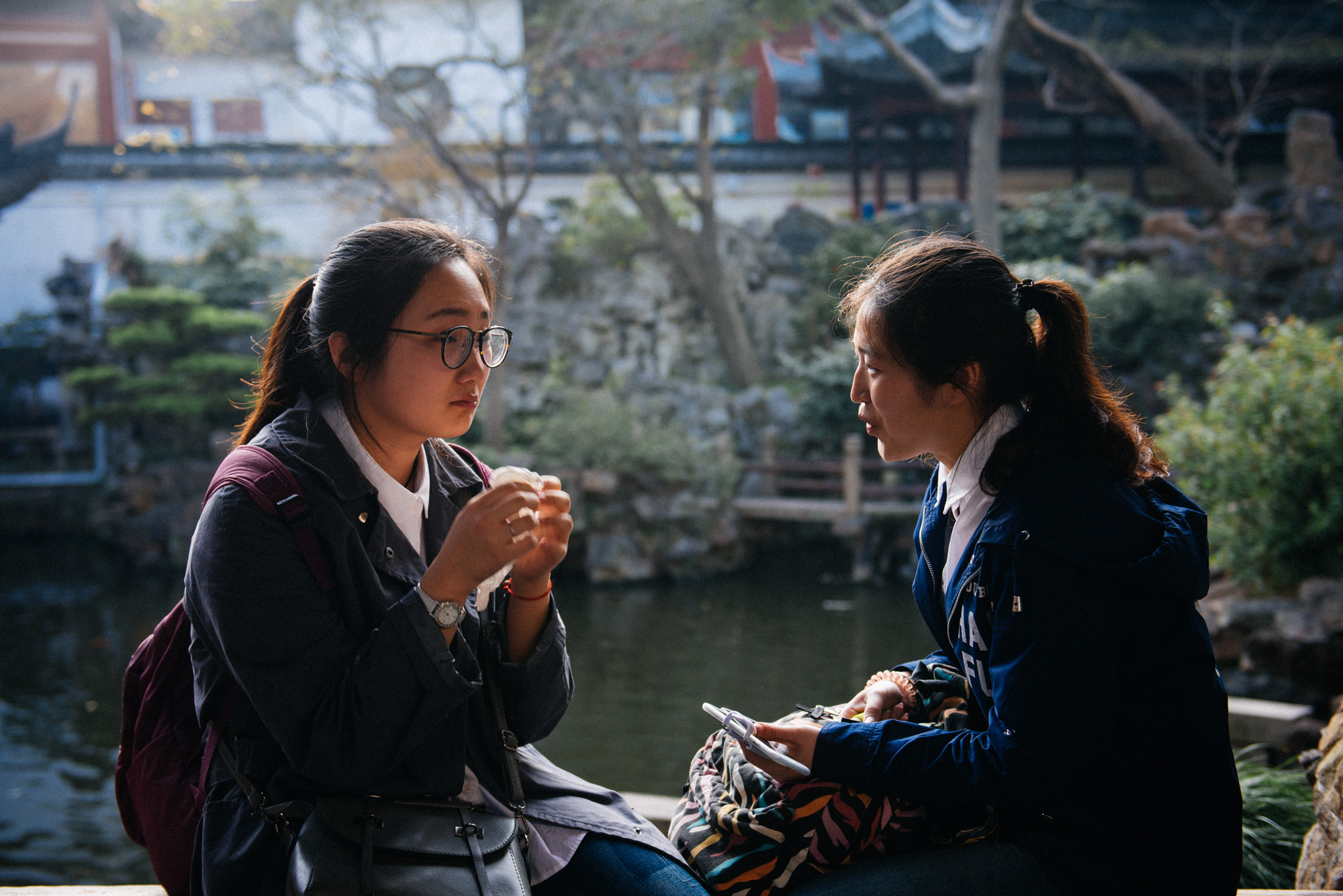Girl cries sitting on a bridge while a friend talks to her as the sound of water from the artificial lake below hides from the dozens of tourists walking by whatever they were saying.
