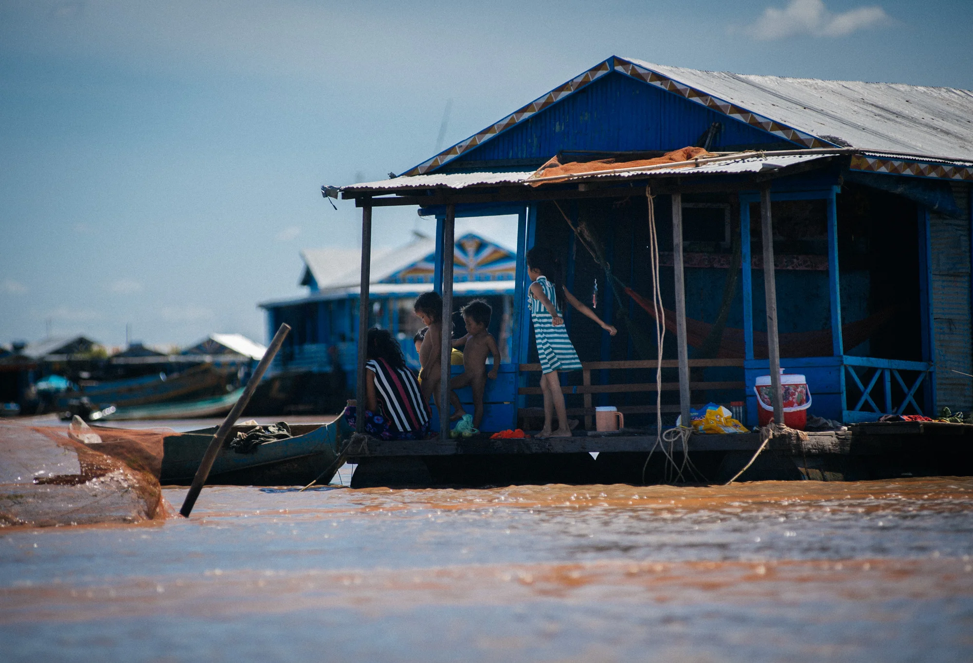 Children play outside their house as the adults rest in hammocks inside.