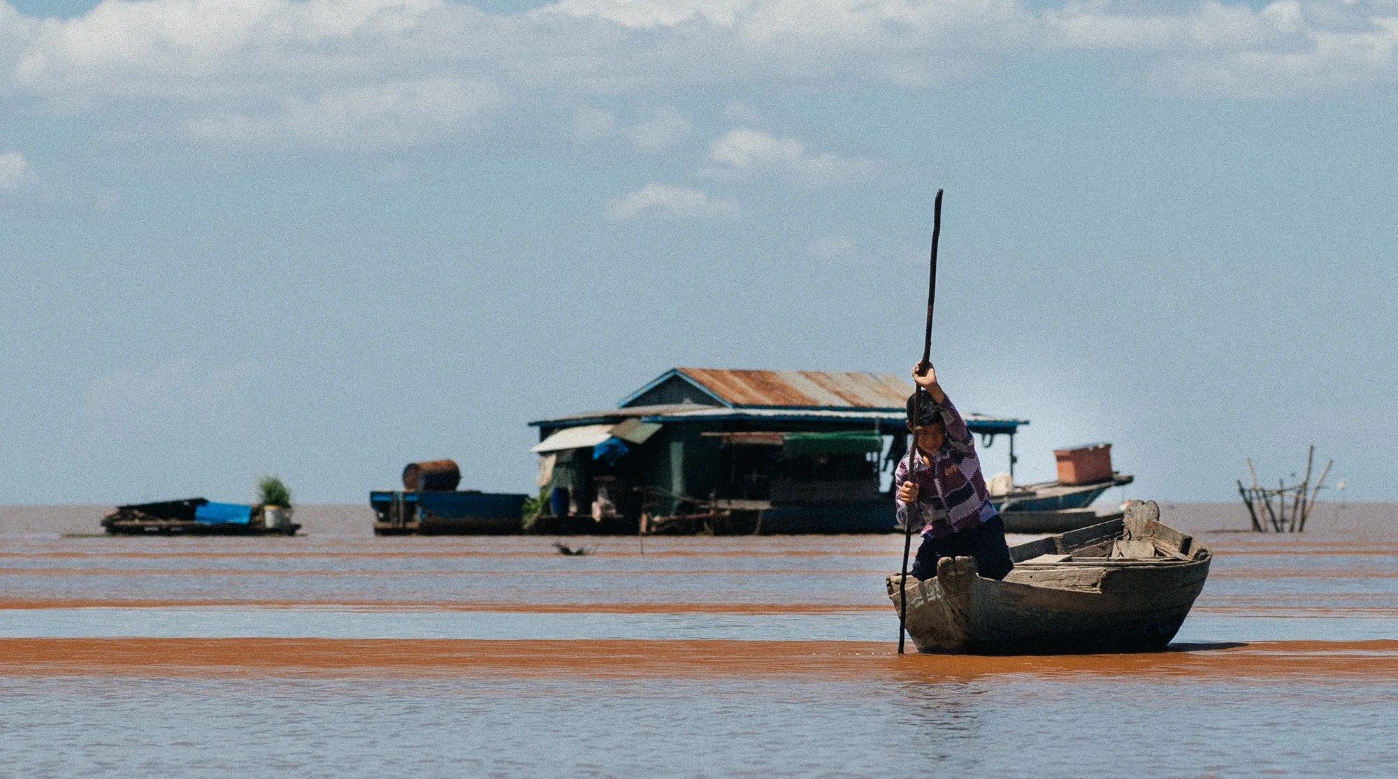 A boy pushes his boat through the shallow water.
