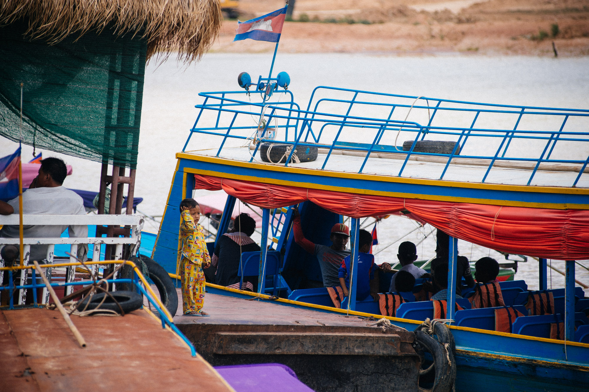 Child looks at large boat with tourists docked on the Siem Reap river margin.