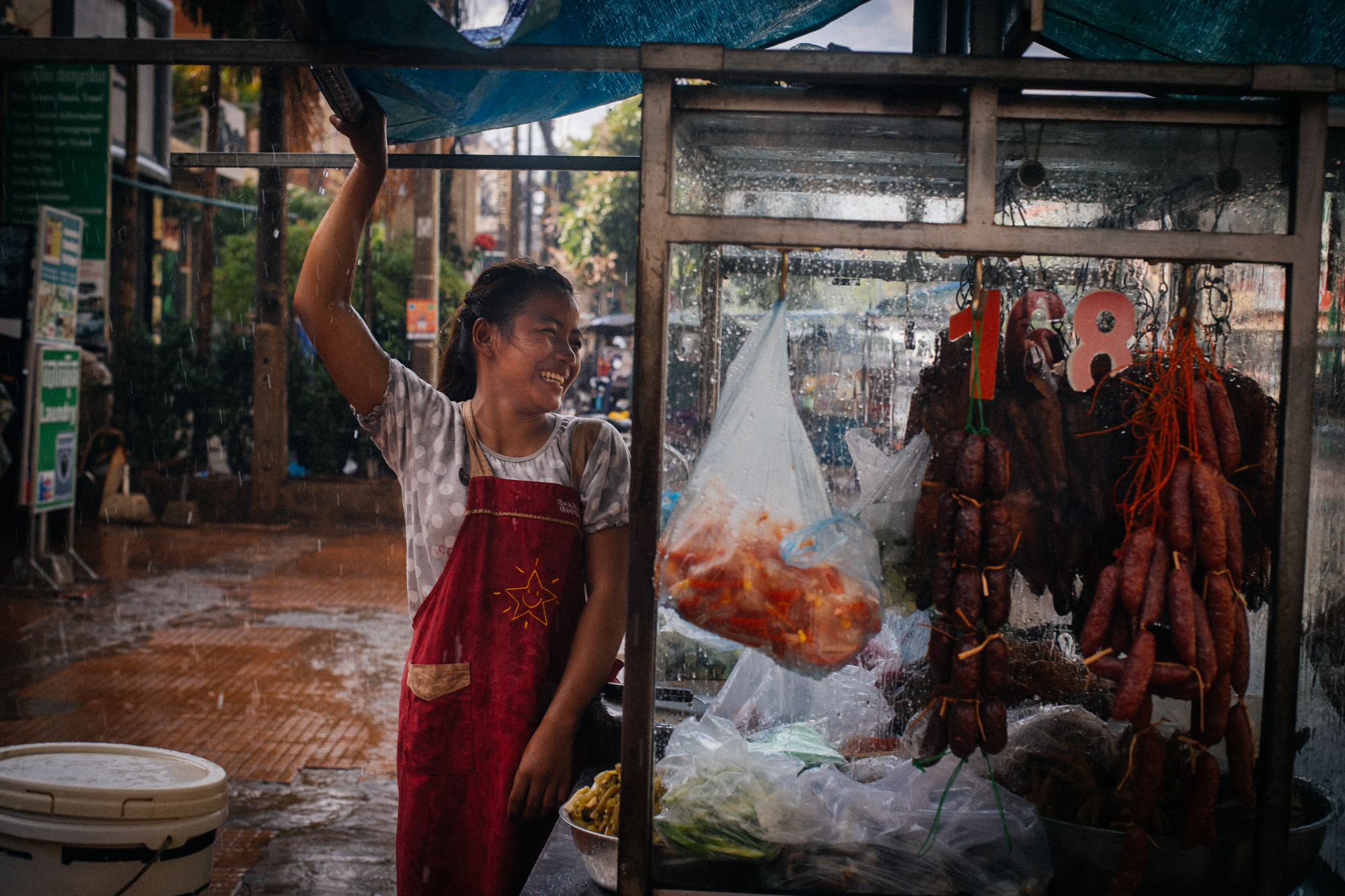 Street vendor talks to her colleague while both protect themselves and the food from the pouring rain in downtown Siem Reap.