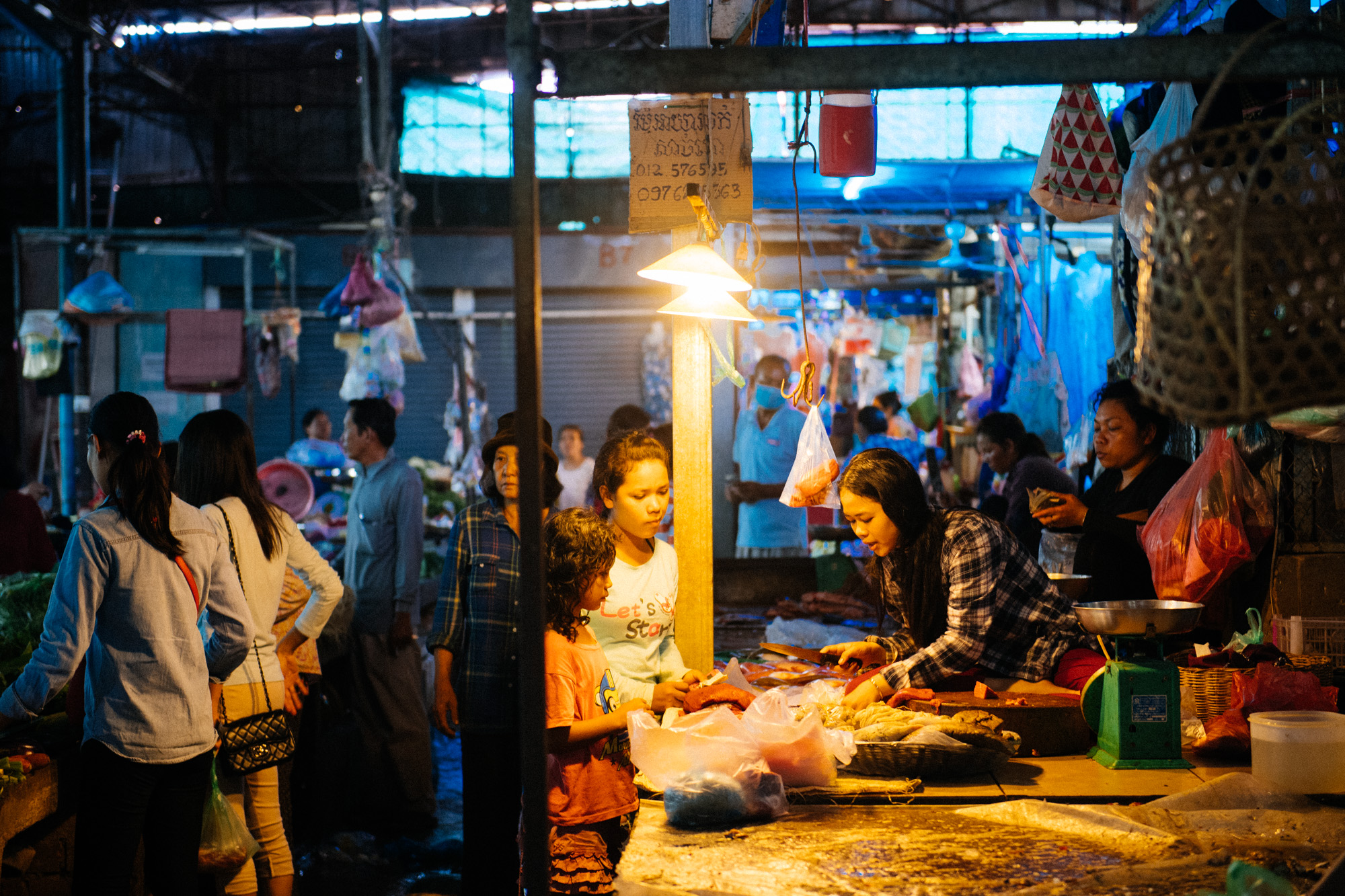 Sitting on the same platform she cuts meat on, woman selects produce to sell to customers.