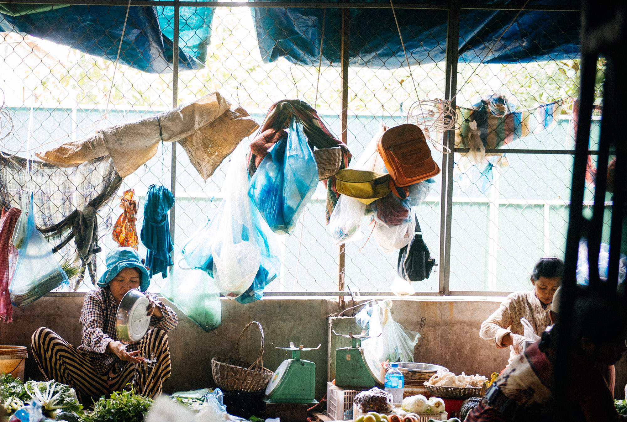 Vendor pour water on her vegetables as her booth neighbor takes a nap on the hammock.