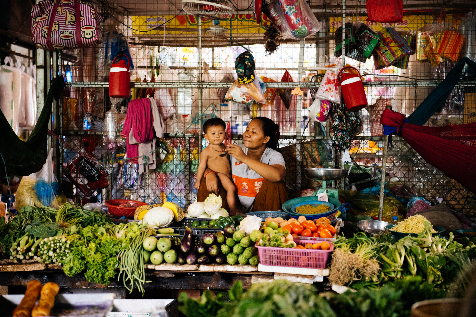 Vendor feeds her son under a fan in the humid and extremely hot market.