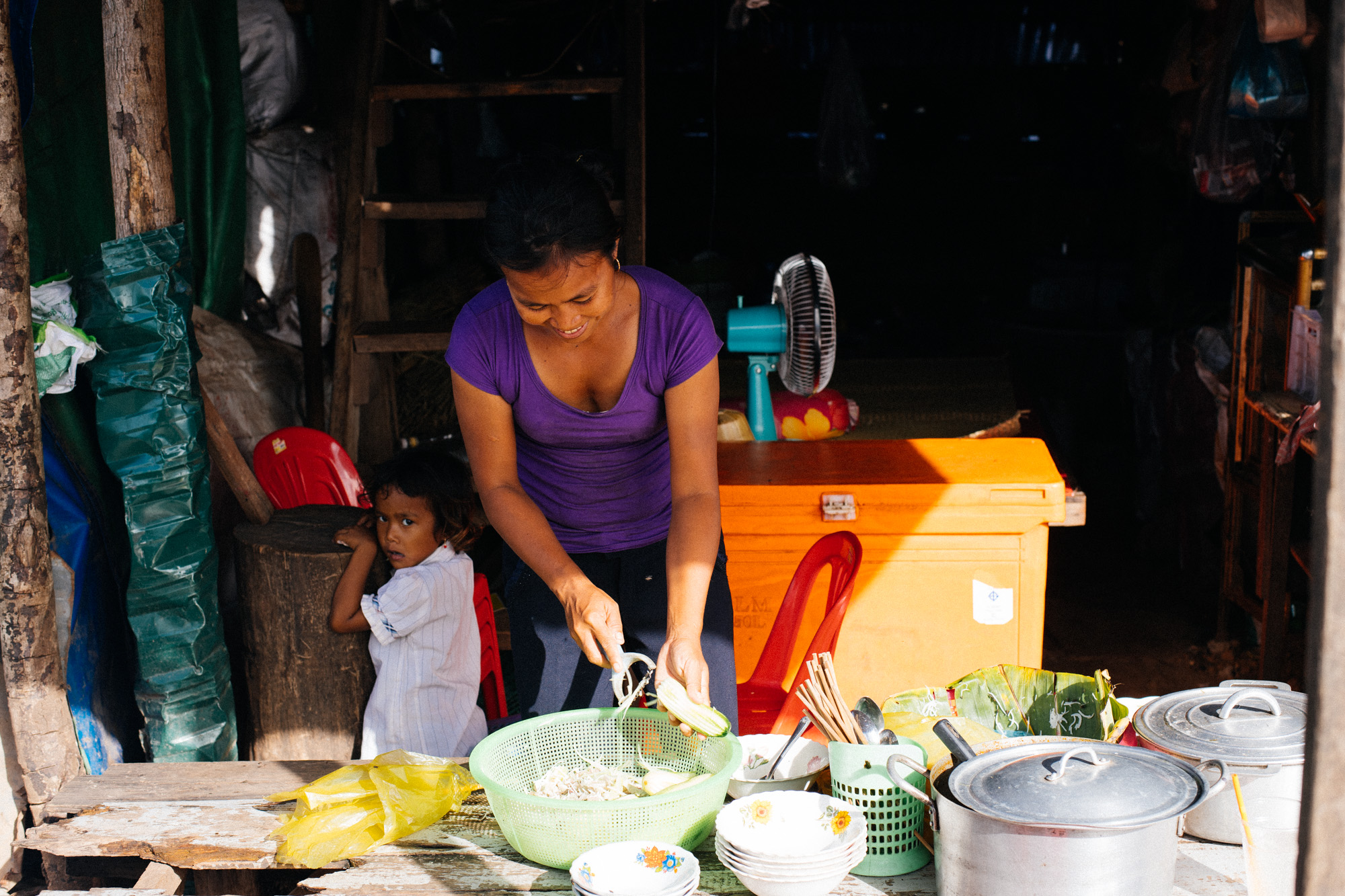 Girl hides behind woman cooking food to sell. Some people would stop by on their scooters to buy food and take home.