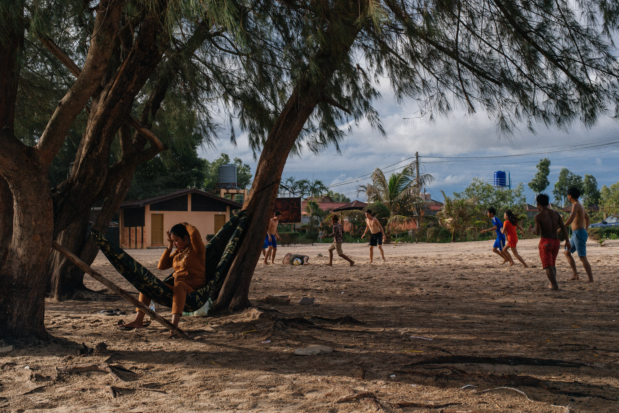 A group of teenagers play football and barbecue seafood on the sand.