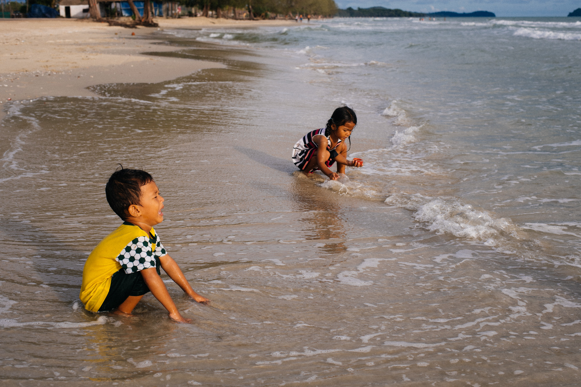 Tourists play in the water. The boy seems he's not liking it.