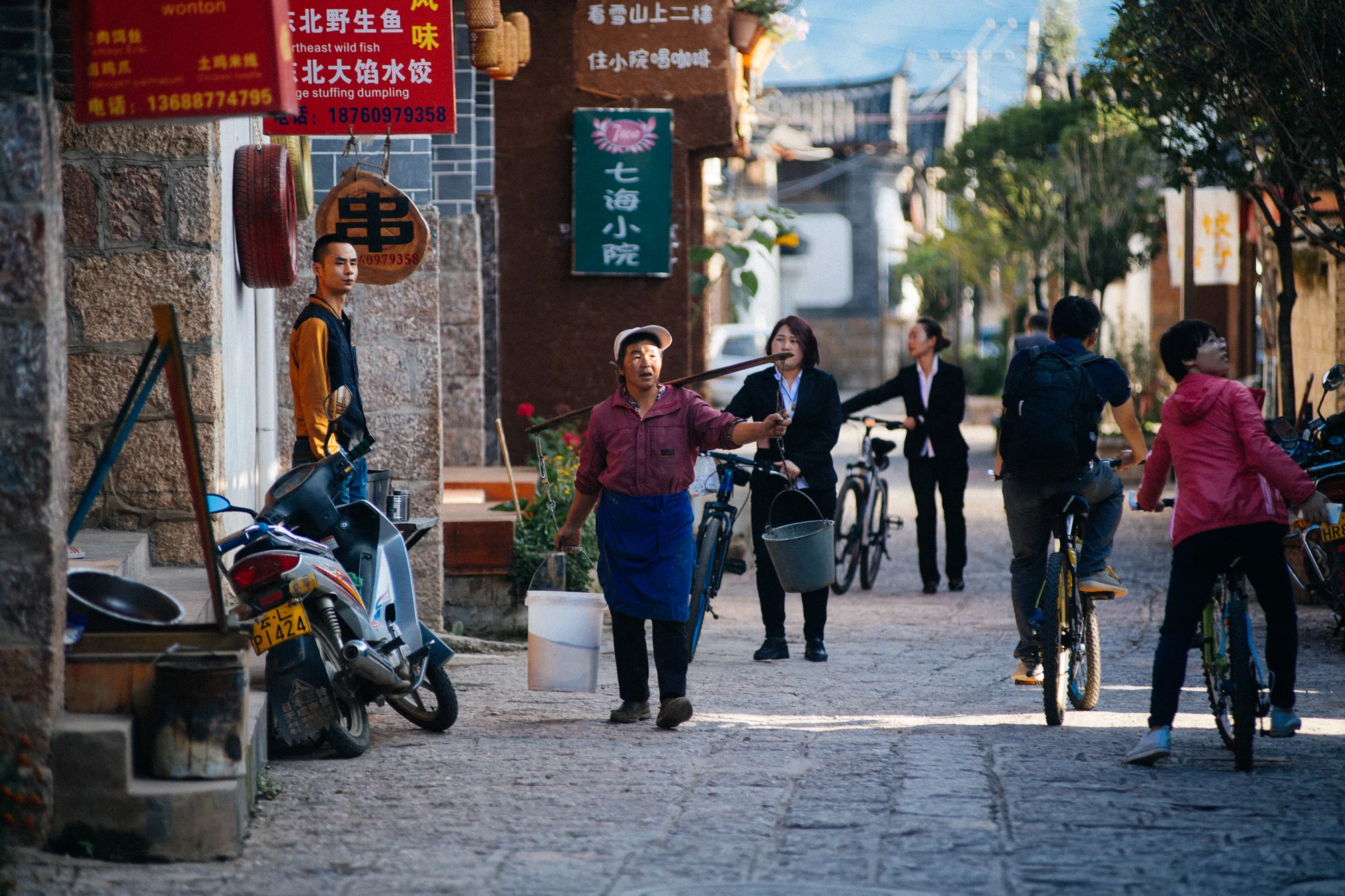 Woman carries two buckets of water while two other women, dressed in a more modern fashion, head back to work, most likely at the restaurants close to the frescoes where all the tourists are taken.