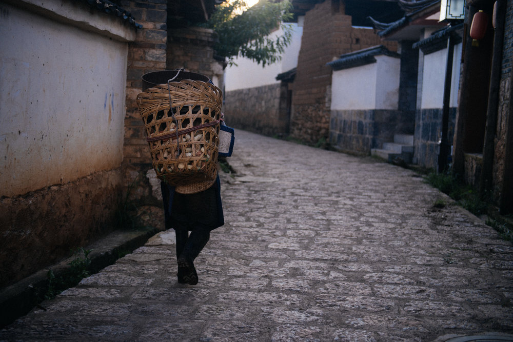  A bit before sunset, a Naxi woman returns home with a basket full of corn. 