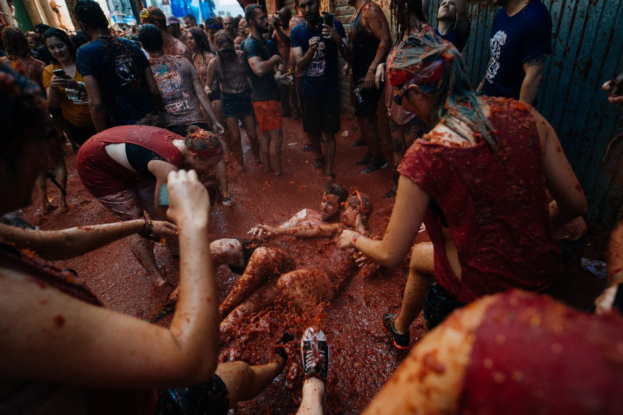 Selfie time. A couple lies in the tomato river while others throw goo on them for a picture.